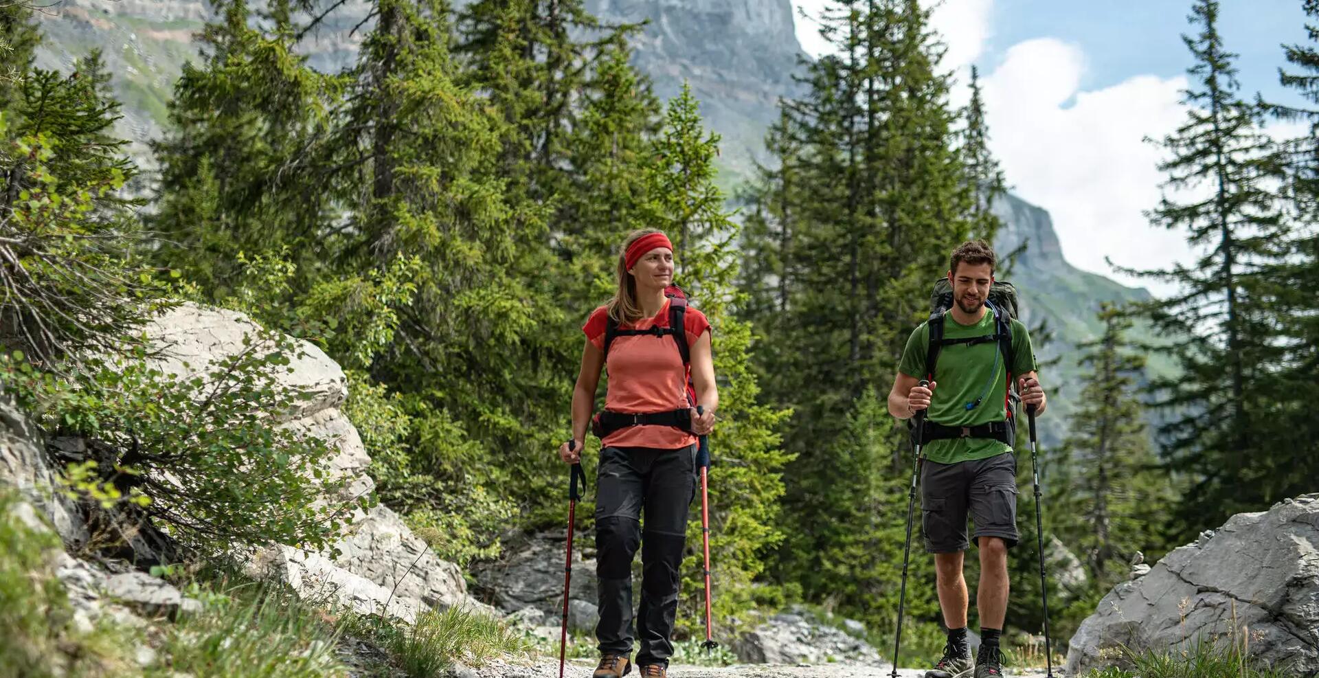mężczyzna i kobieta wędrujący szlakiem górskim w odzieży trekkingowej z kijami trekkingowymi w rękach