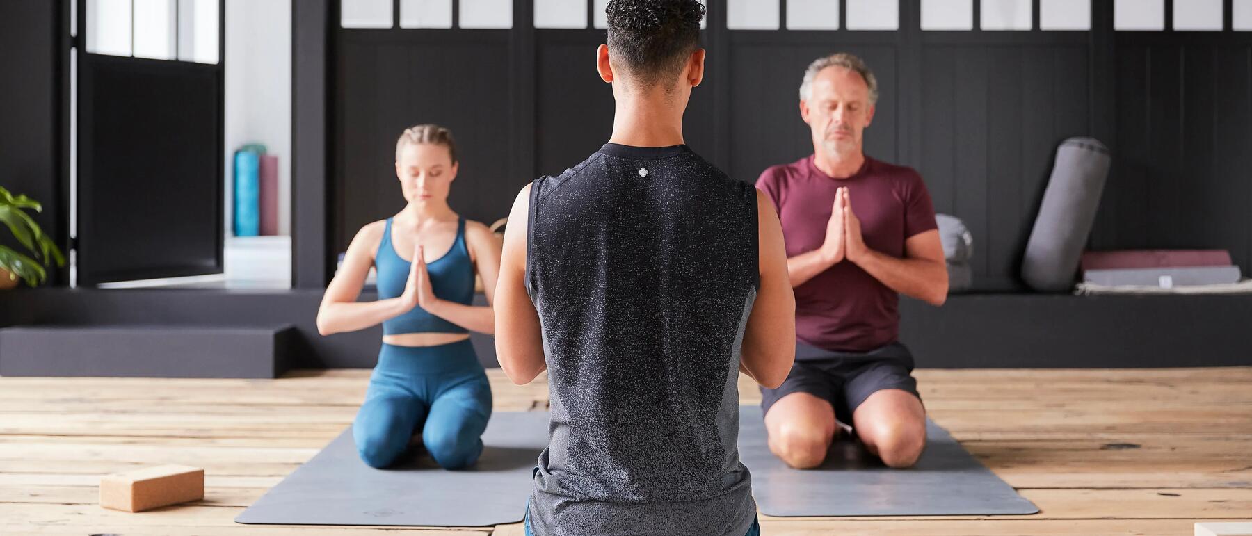 Bild von zwei Männern und einer Frau, die Yoga machen. Einer der Männer ist der Trainer.