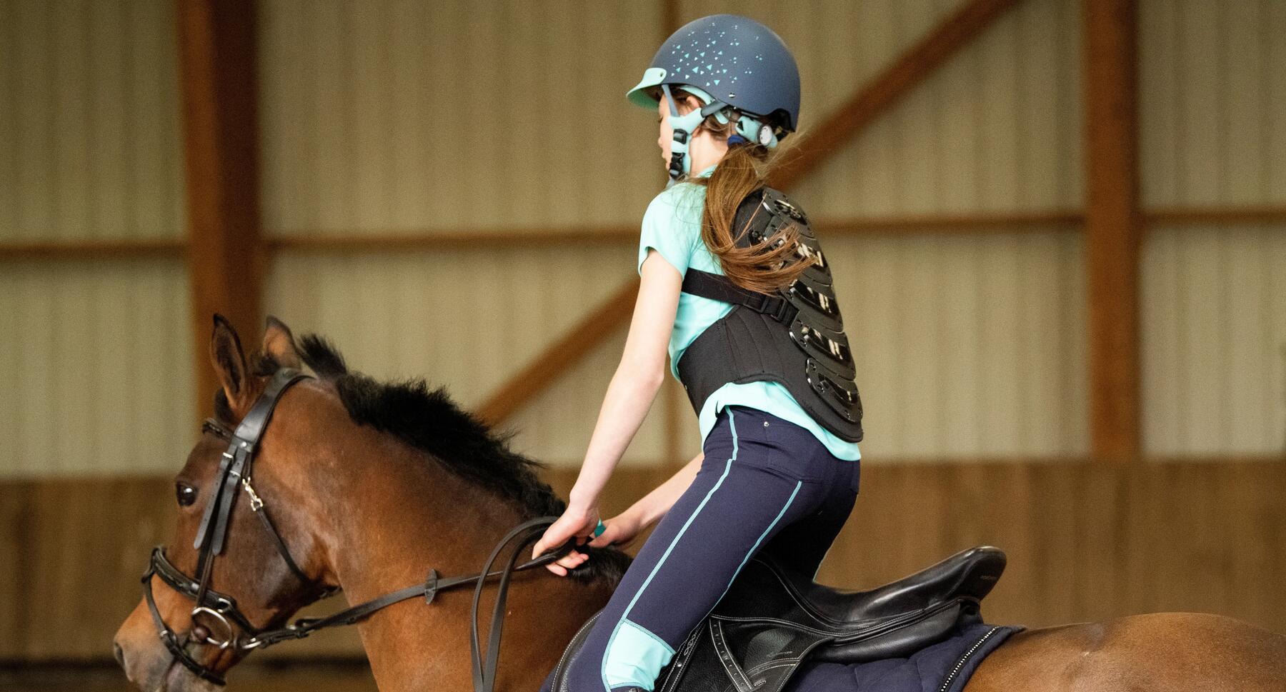 Kind reitet auf einem Pferd und trägt eine Reitschutzweste