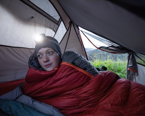 kobieta leżąca w śpiworze w namiocie z latarką czołową na głowie