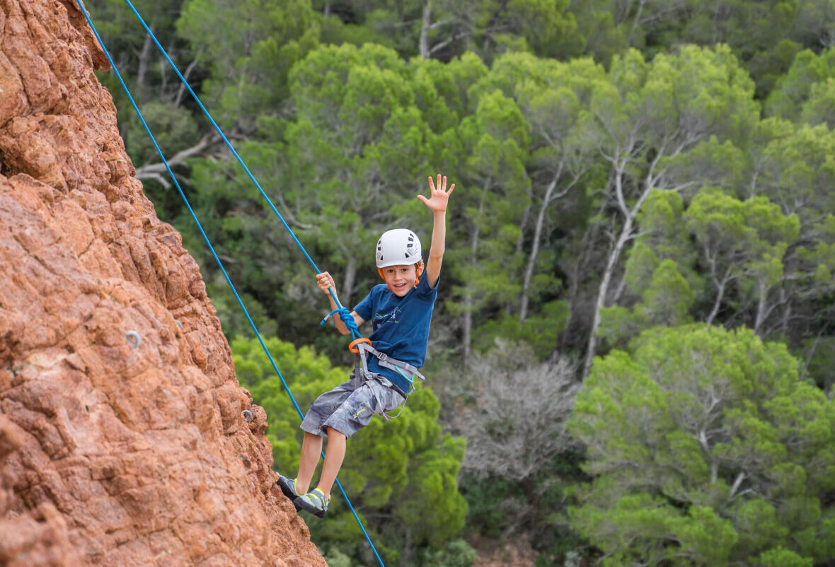 petit garçon escaladant une falaise estérieuresouriant et saluant de la main