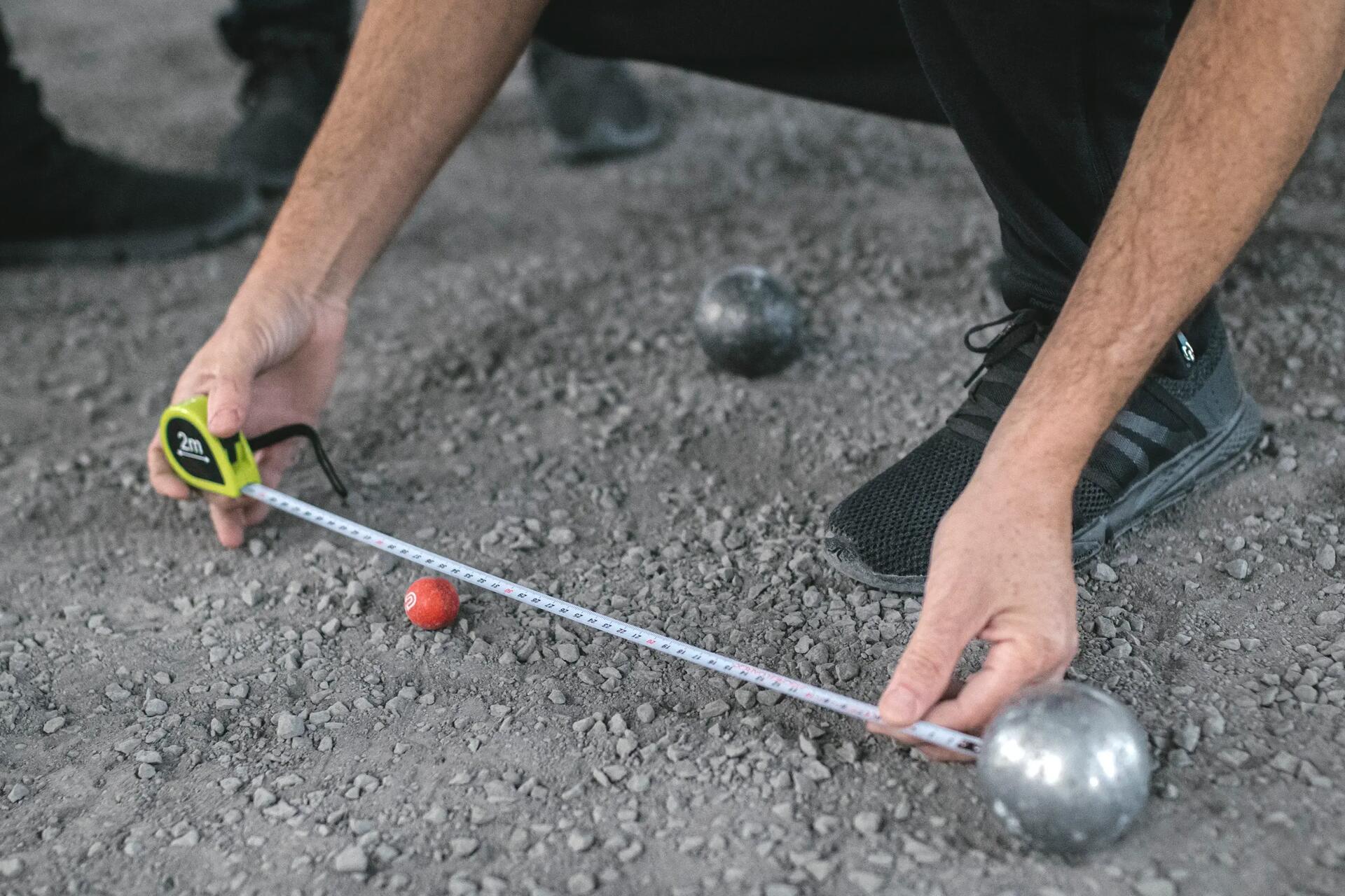 Iemand meet de afstand van een boule tot het butje bij petanque