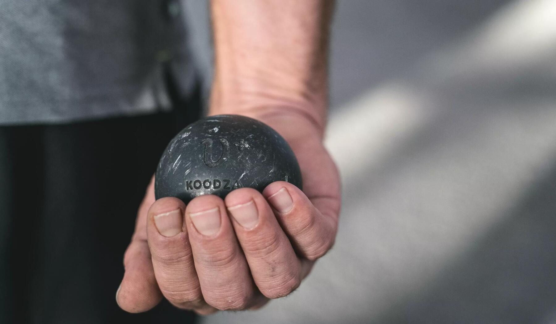 Mann hält in seiner rechten Hand eine schwarze Boulekugel 