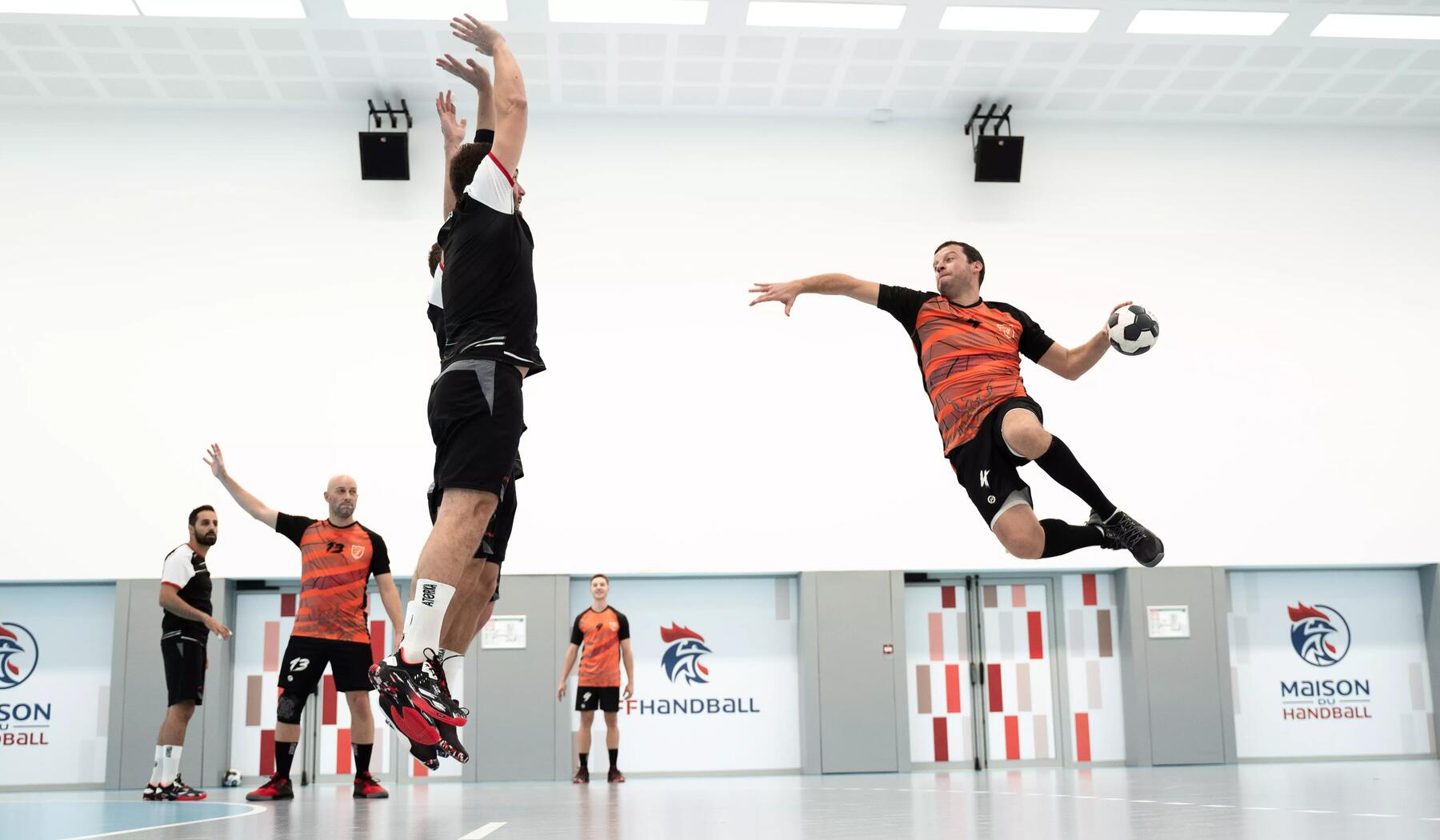 Mann springt hoch und setzt zum Wurf mit dem Handball an. Sein Gegenspiel versucht ihn den Wurf zu blocken