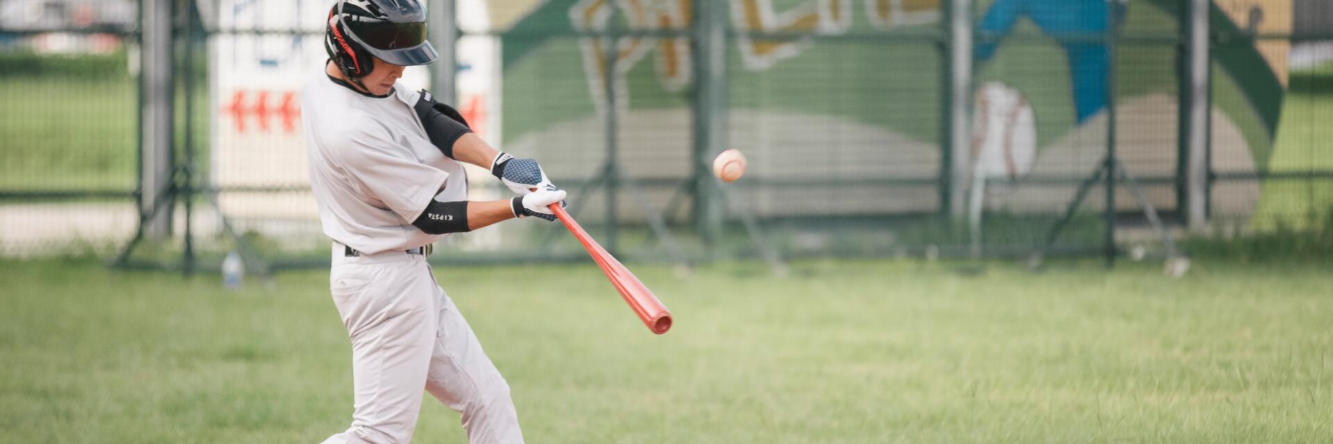 Zawodnik w rękawicach baseballowych odbijający piłkę baseballową kijem do baseballa stojąc na boisku