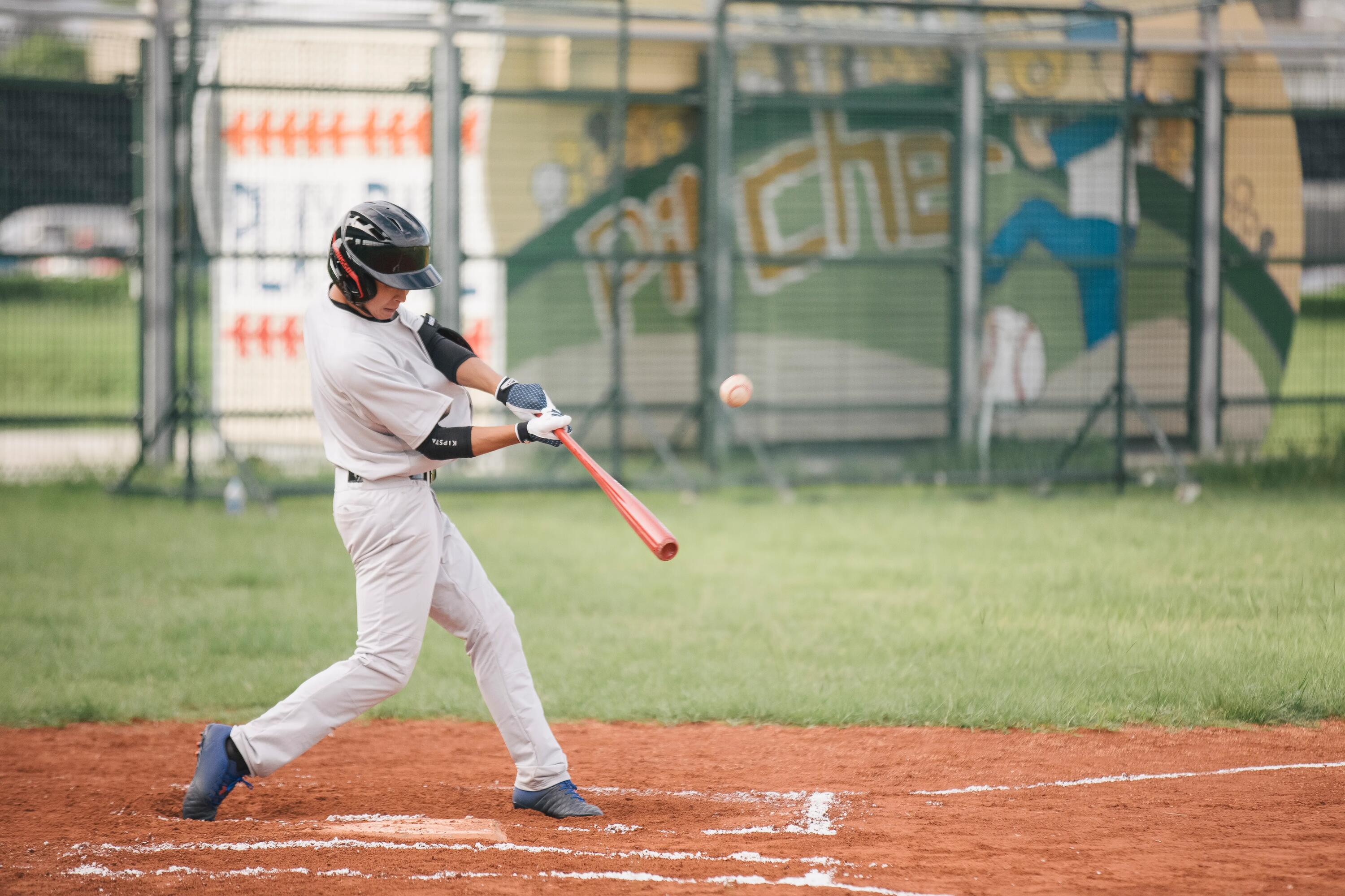 Zawodnik w rękawicach baseballowych odbijający piłkę baseballową kijem do baseballa stojąc na boisku