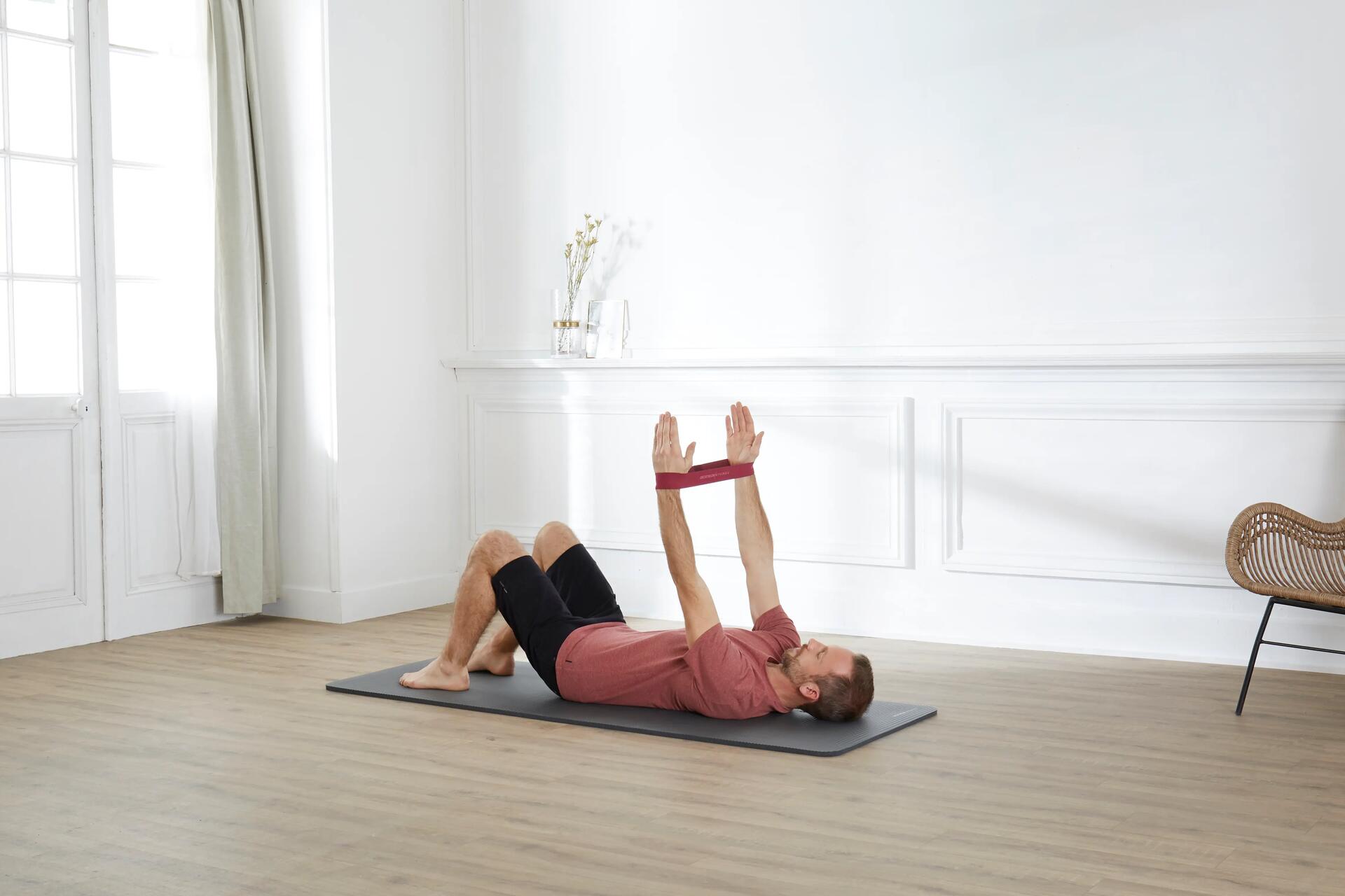 Mężczyzna ćwiczący pilates na macie z gumą na rękach w domu