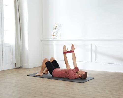 Mężczyzna ćwiczący pilates leżąc na macie z gumami założonymi na ręce