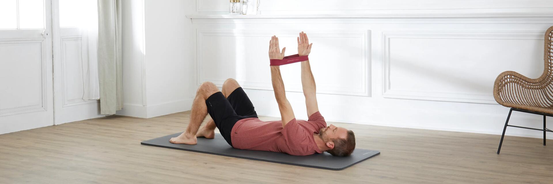 Mężczyzna ćwiczący pilates leżąc na macie z gumami założonymi na ręce