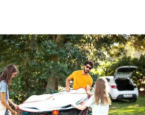 Two women and a man carrying pop-up tent towards car