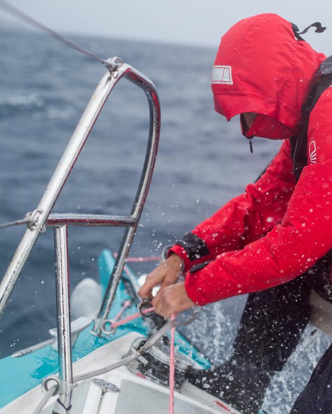 Een man en vrouw met automatisch reddingsvest aan zitten op de rand van de zeilboot te genieten van het uitzicht