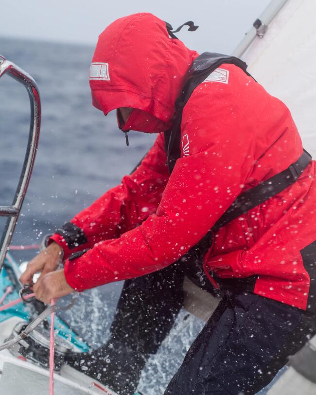 Een man en vrouw met automatisch reddingsvest aan zitten op de rand van de zeilboot te genieten van het uitzicht