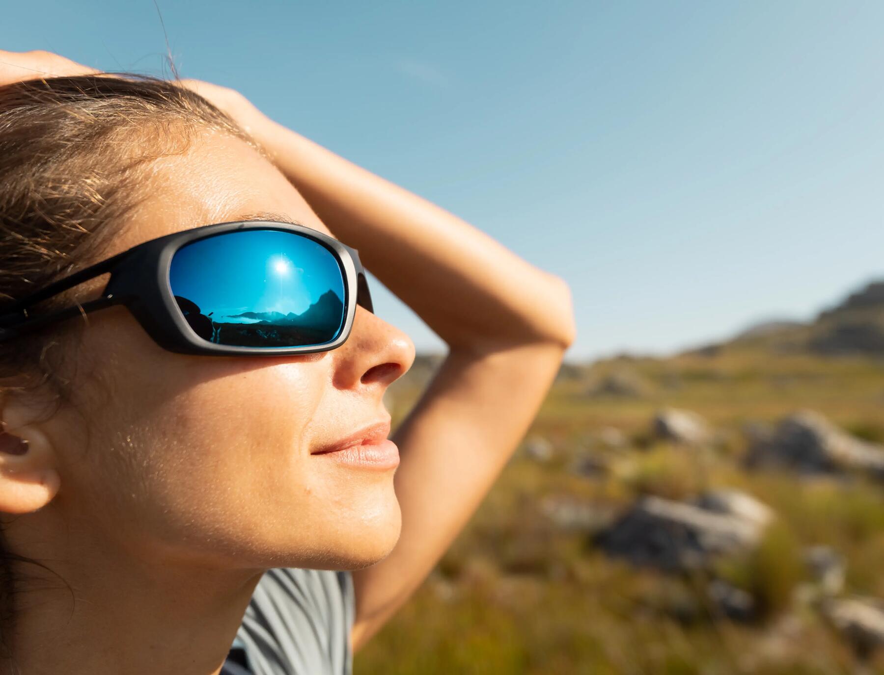 Frau trägt Sonnebrille und schaut der Sonne entgegen