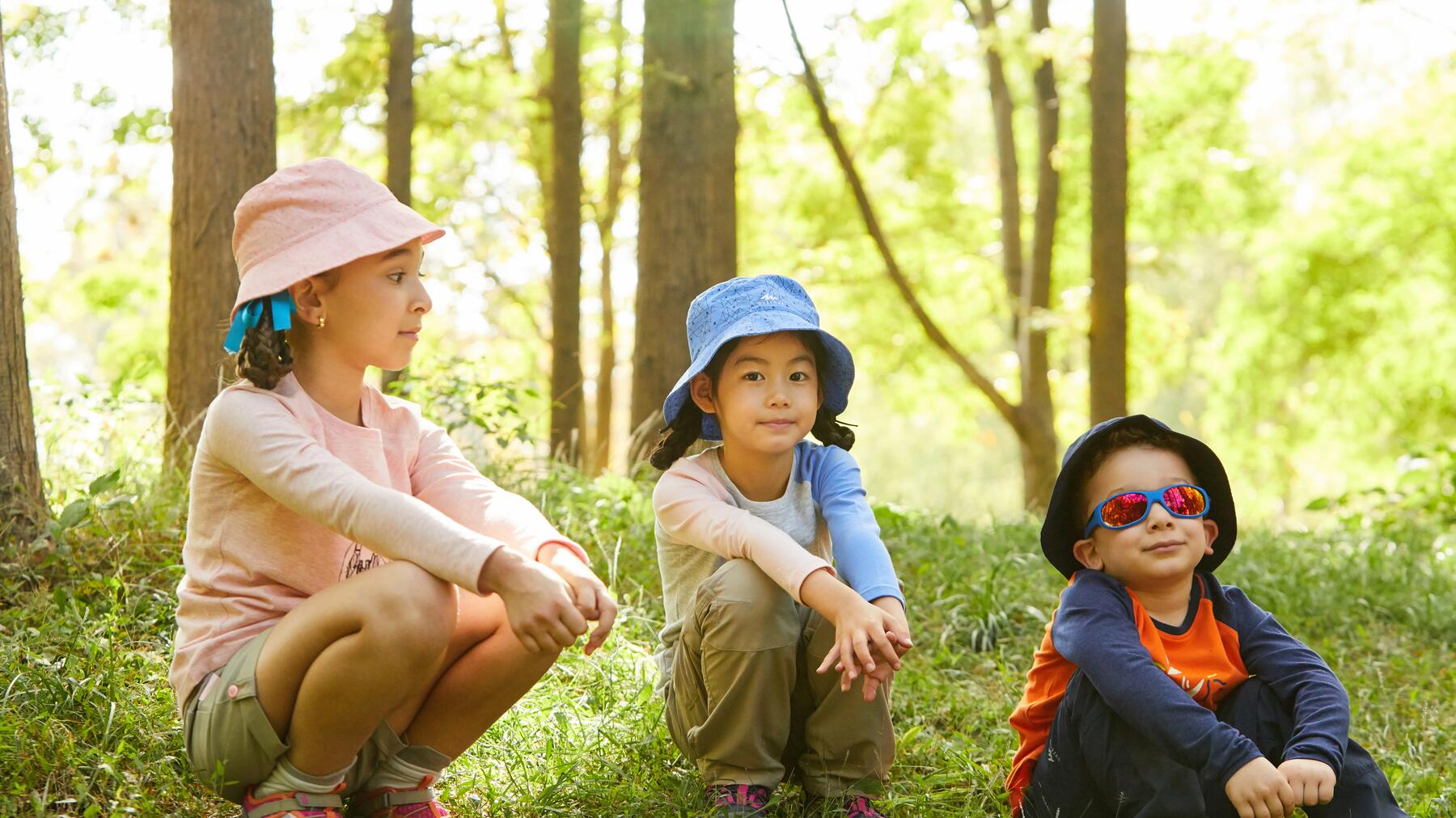 Drei Kinder sitzen mit Wanderschuhen im Wald