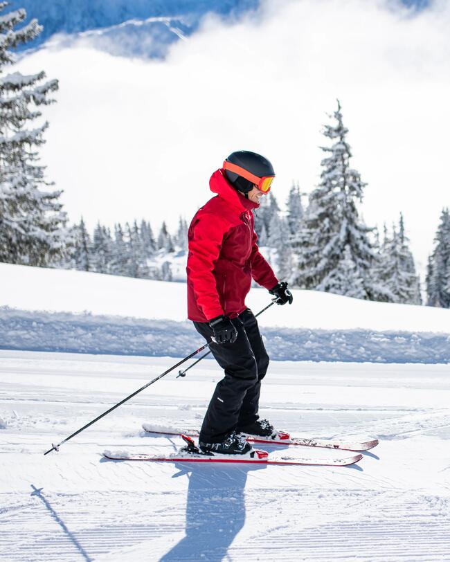 Ein Mann mit schwarzer Skihose und roter Skijacke fährt auf einer flachen Piste Ski-