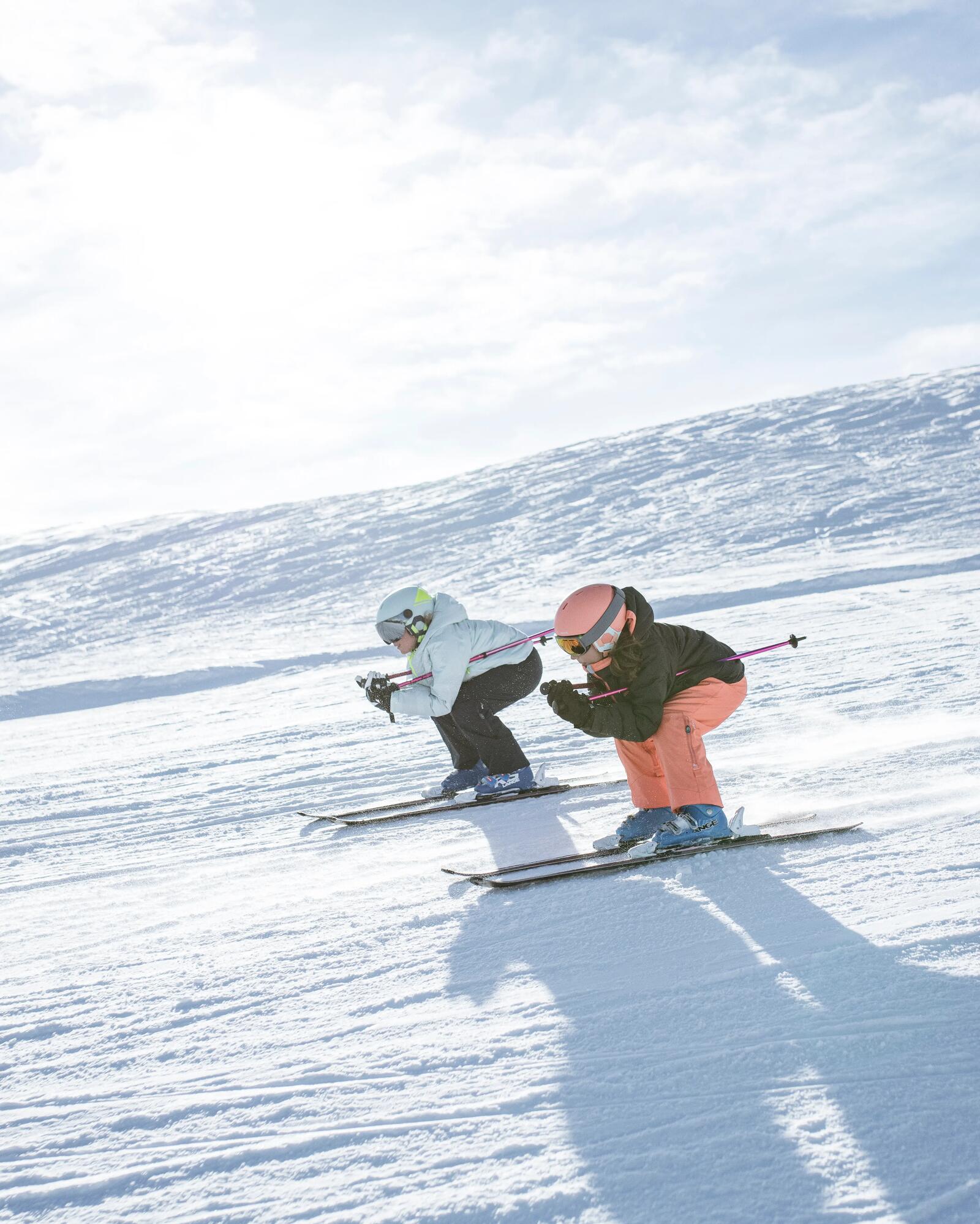 Kinder fahren in Schussposition die Piste auf Skiern hinunter