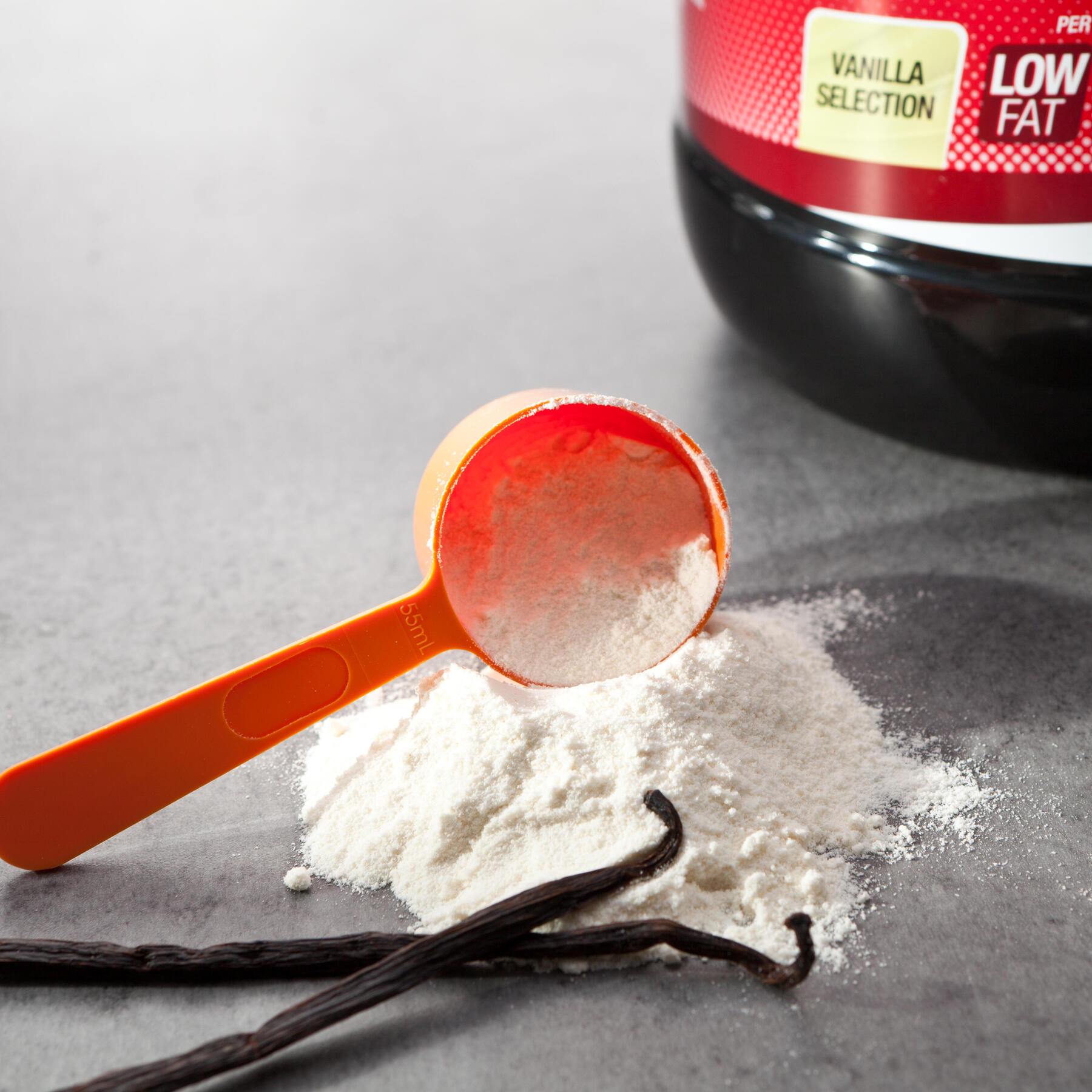 Proteinpulver auf Arbeitsplatte mit Vanilleschoten und einem Messlöffel.