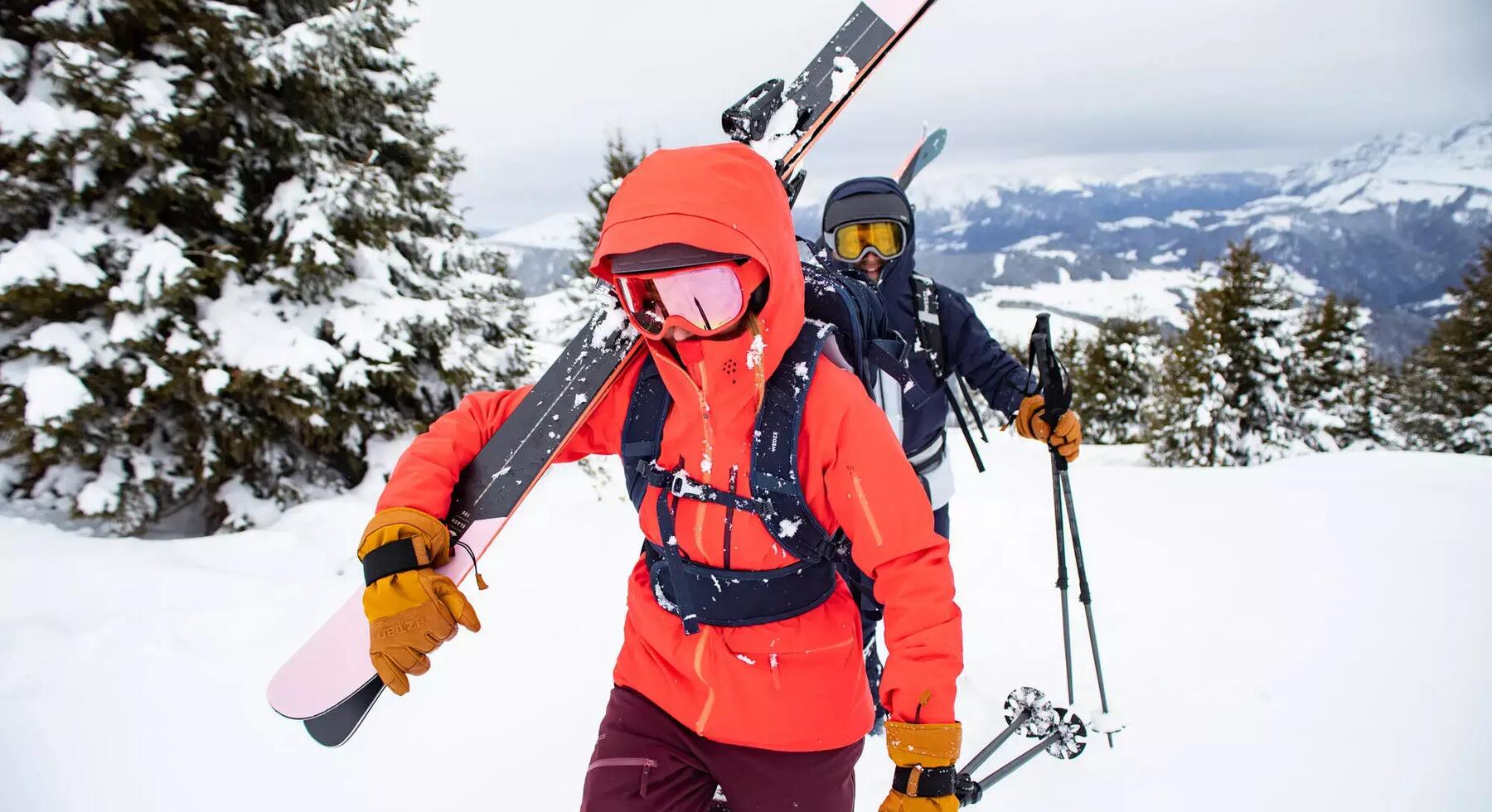 Mann wandert durch den Schnee und trägt Skii auf der Schulter