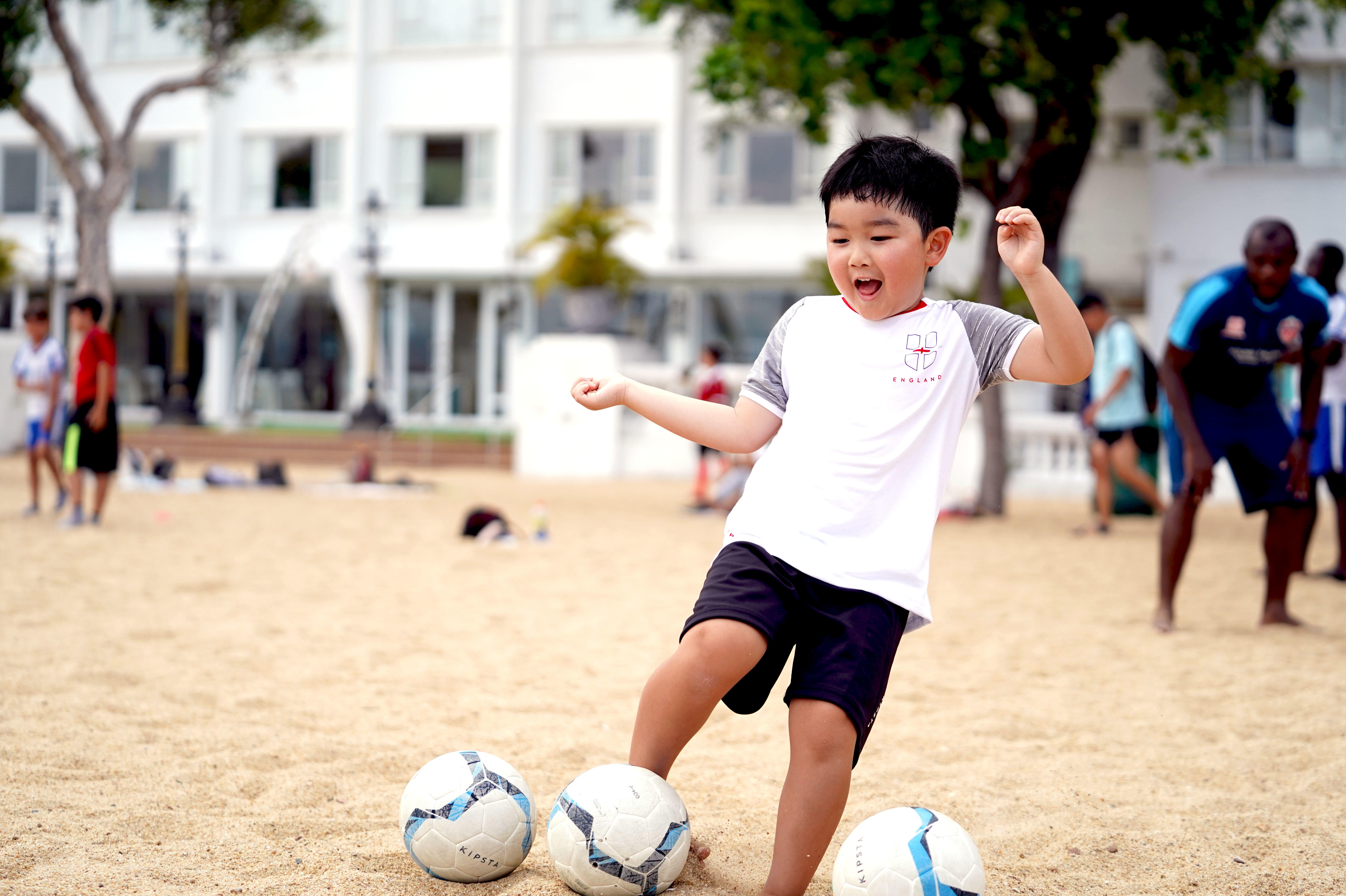 Boy playing with footballs on a sandy beach