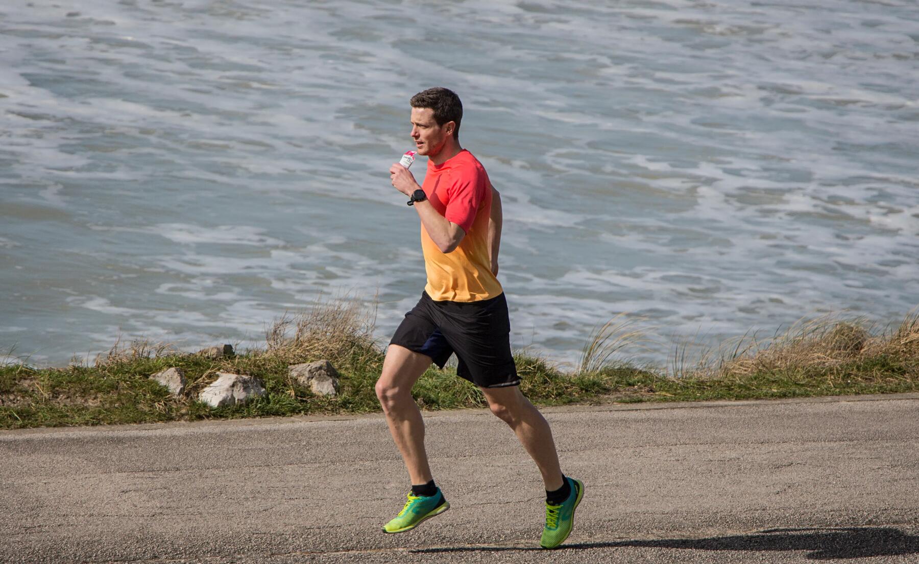 mężczyzna biegnący w odzieży i butach do biegania spożywając żel energetyczny