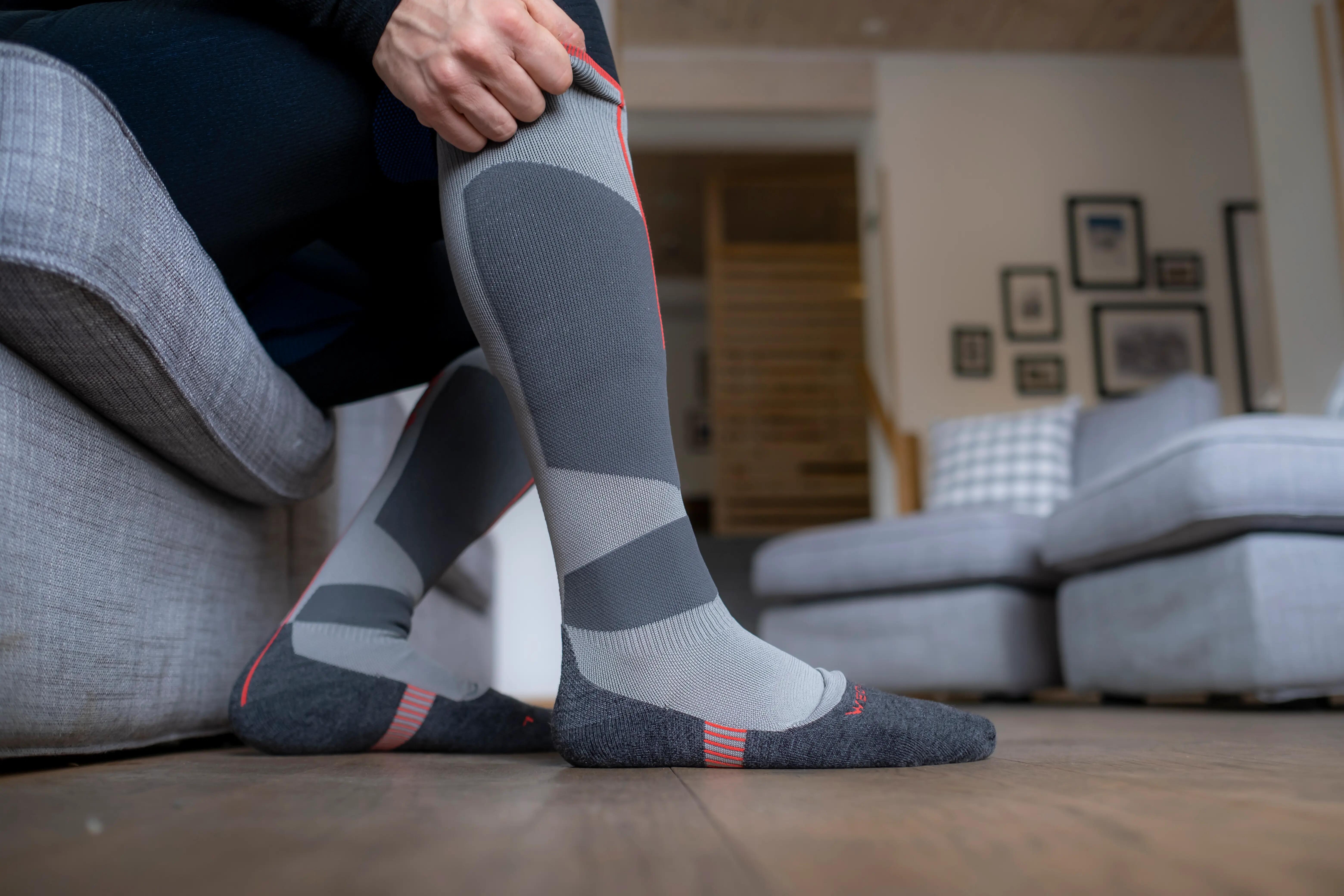Person pulling on grey knee-high ski socks while seated indoors