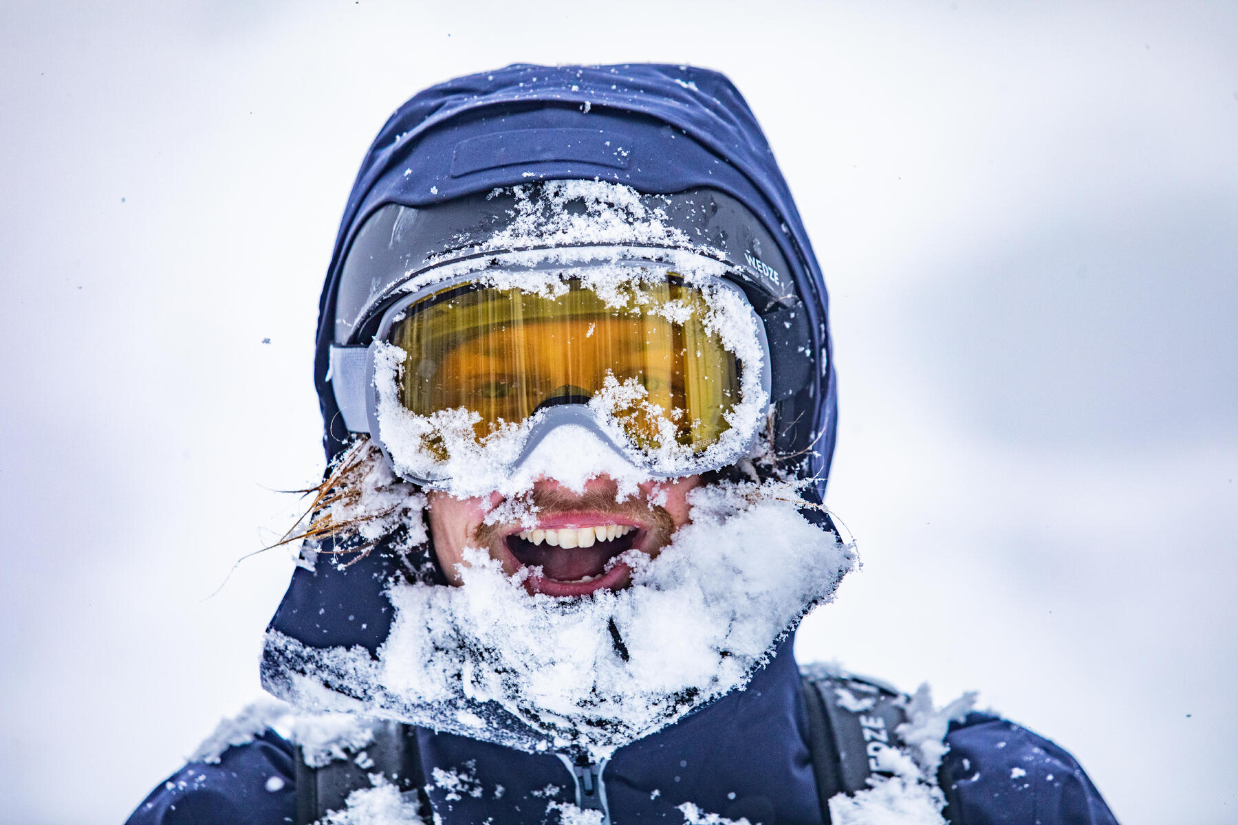 Mann hat Schnee auf der Skibrille und im Gesicht