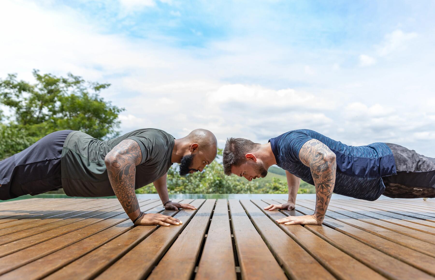 Two guys doing push ups outdoor on a wooden floor
