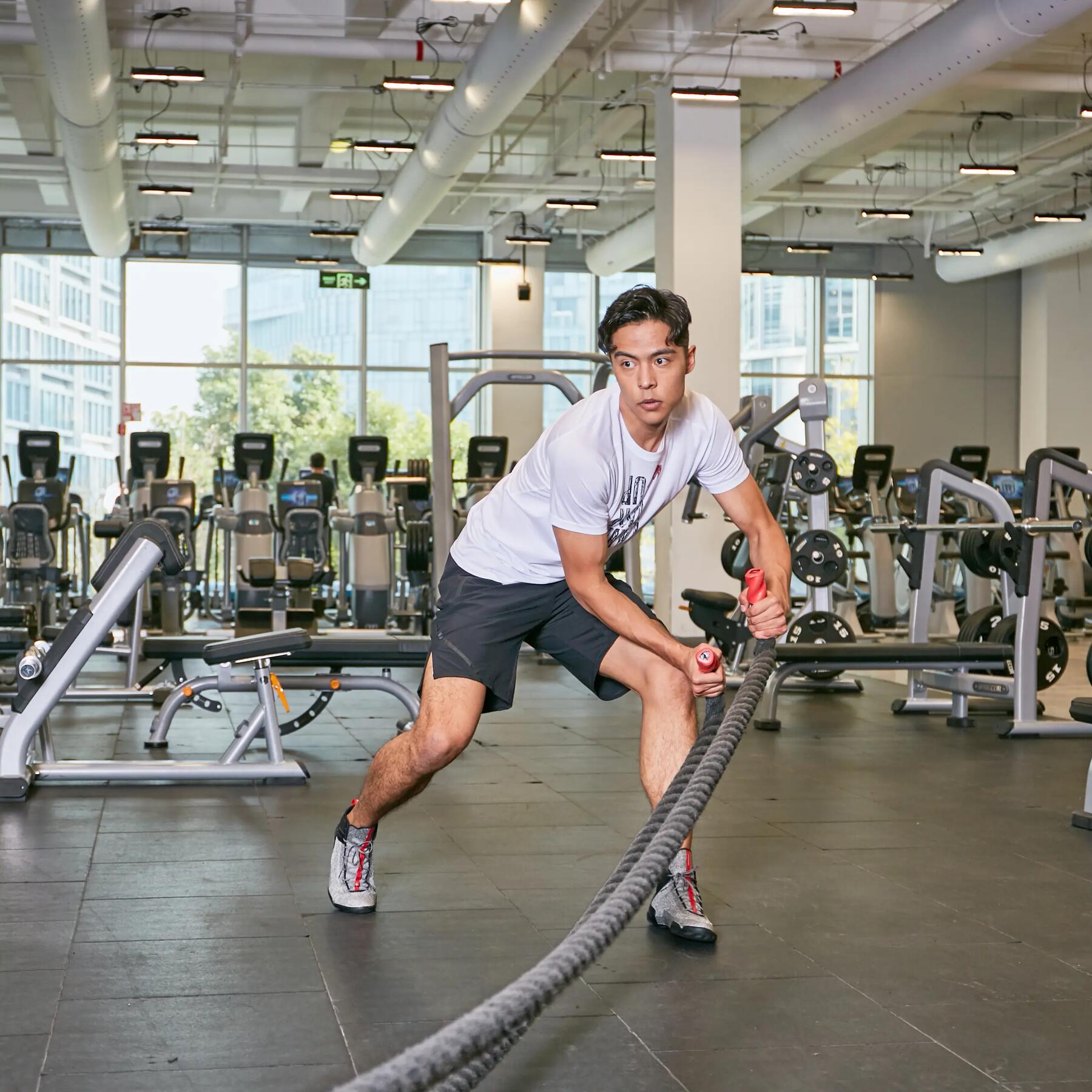 Mężczyzna ćwiczący z linami treningowymi nazywanymi battle ropes na siłowni