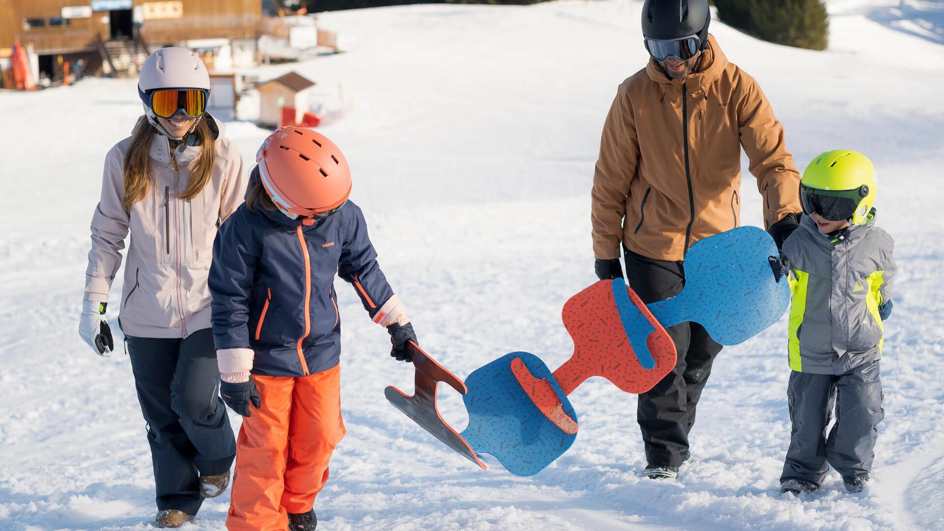 mężczyzna i kobieta idą z dziećmi trzymającymi ślizgi zjazdowe po śniegu 