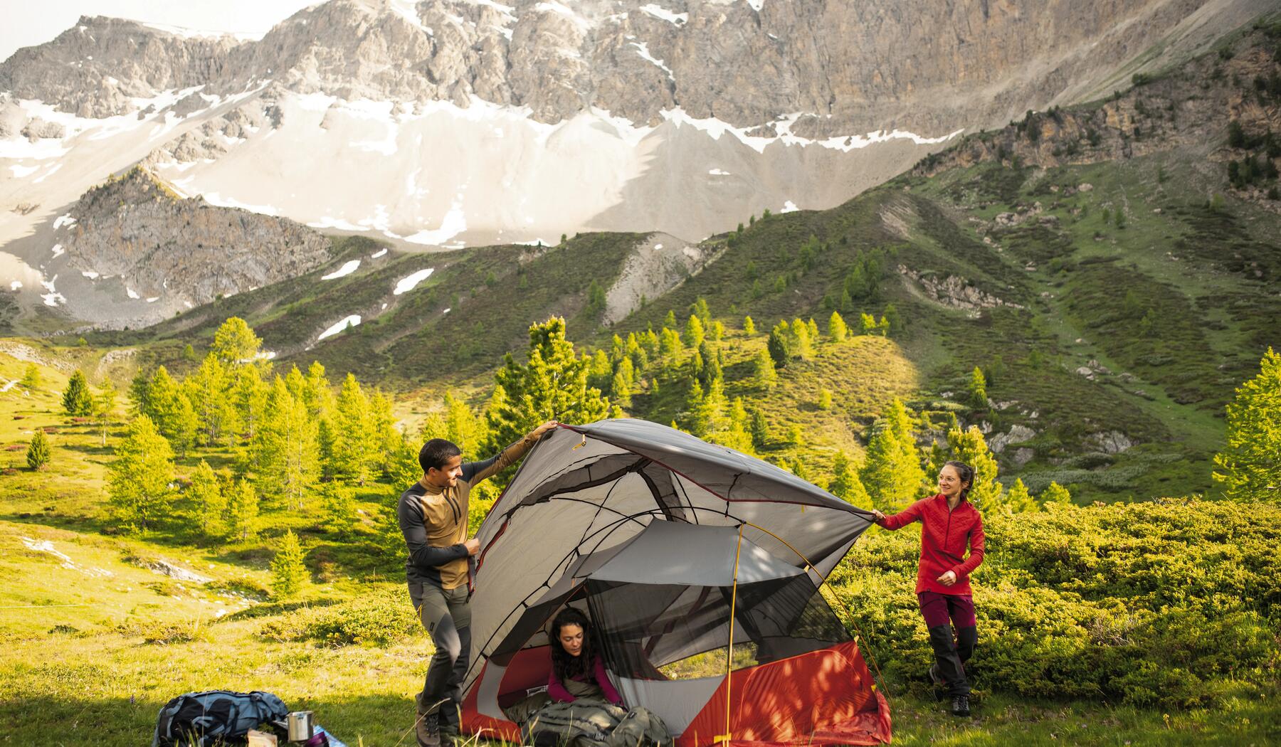 Drei Personen bauen ein Trekkingzelt vor einer Bergkulisse auf