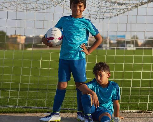 chłopcy w odzieży piłkarskiej stojący w bramce z piłką nożną