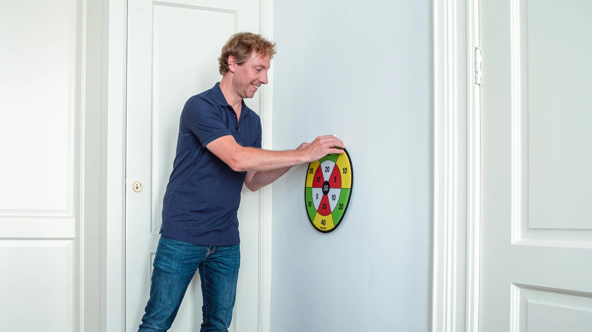 A man setting up a darts practise board for beginners