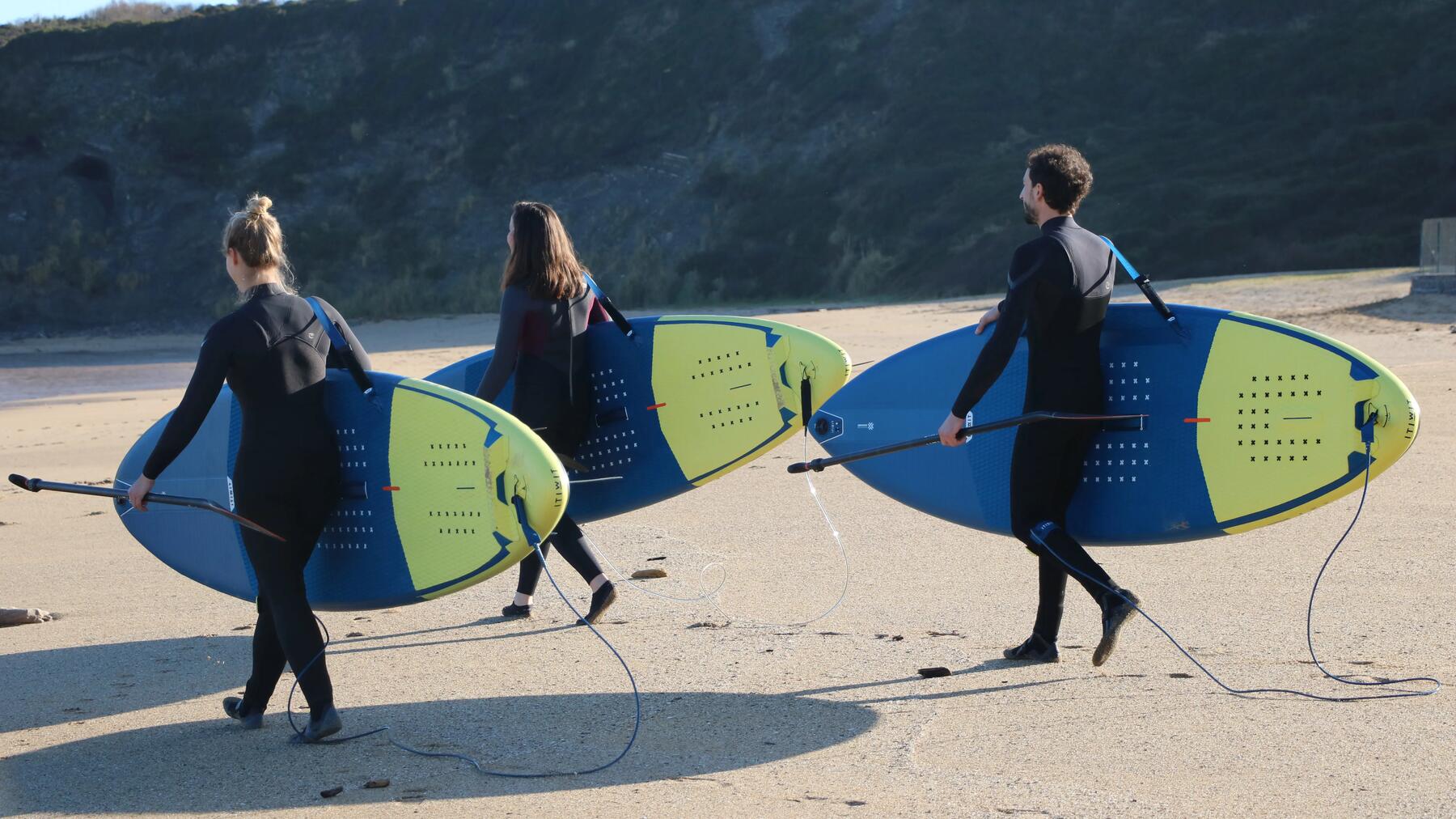 Drei Personen tragen SUP-Bekleidung am Strand