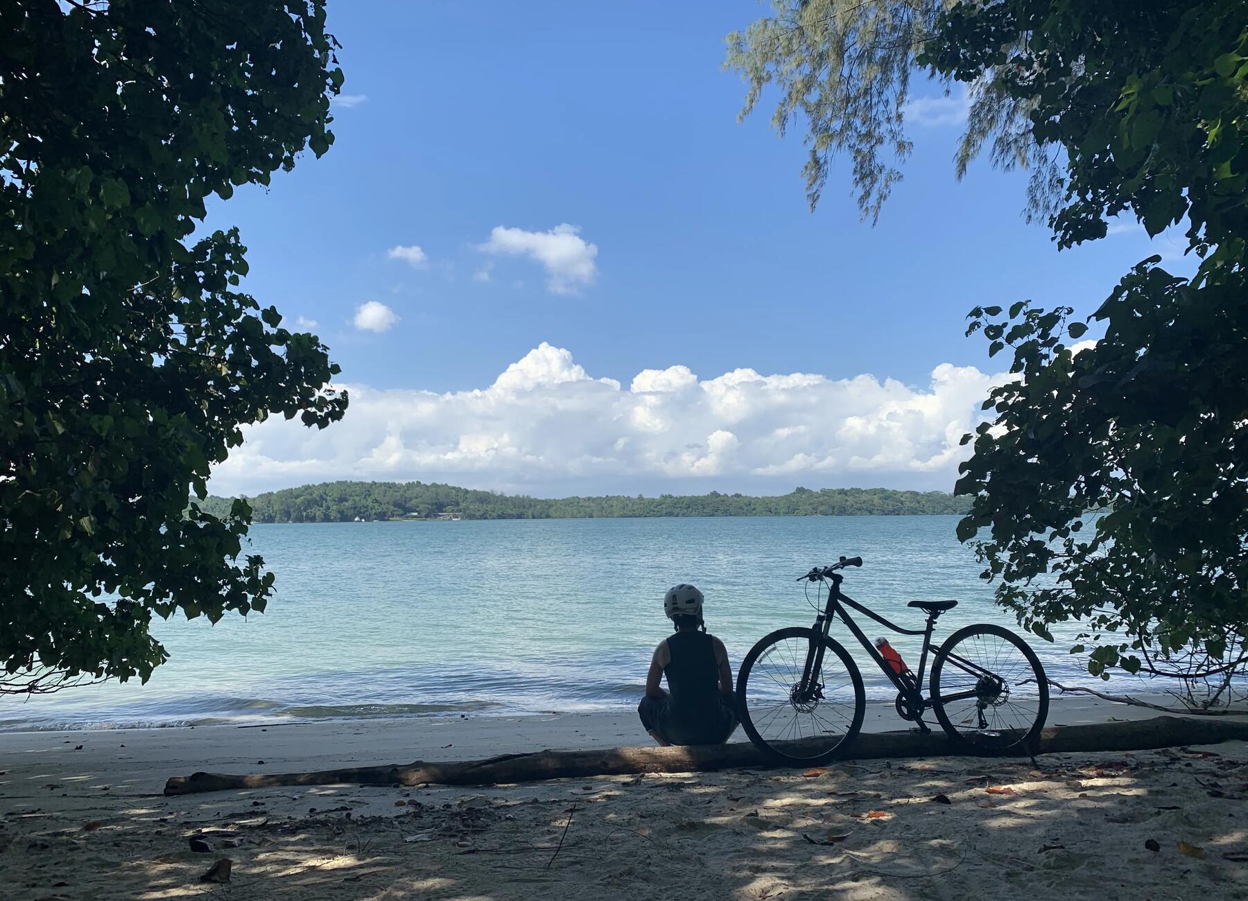 osoba w stroju rowerowym siedząca na plaży przy rowerze