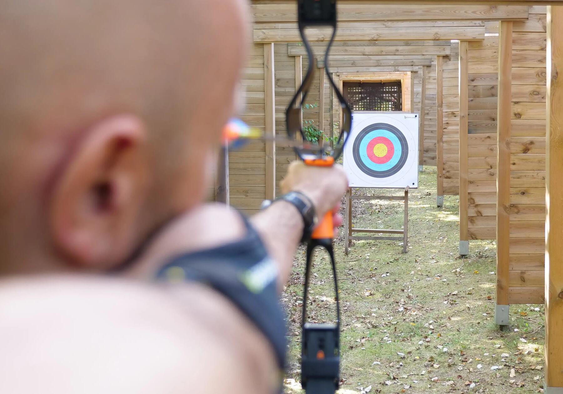 A close of a man focusing his archery bow and arrow at a practise target