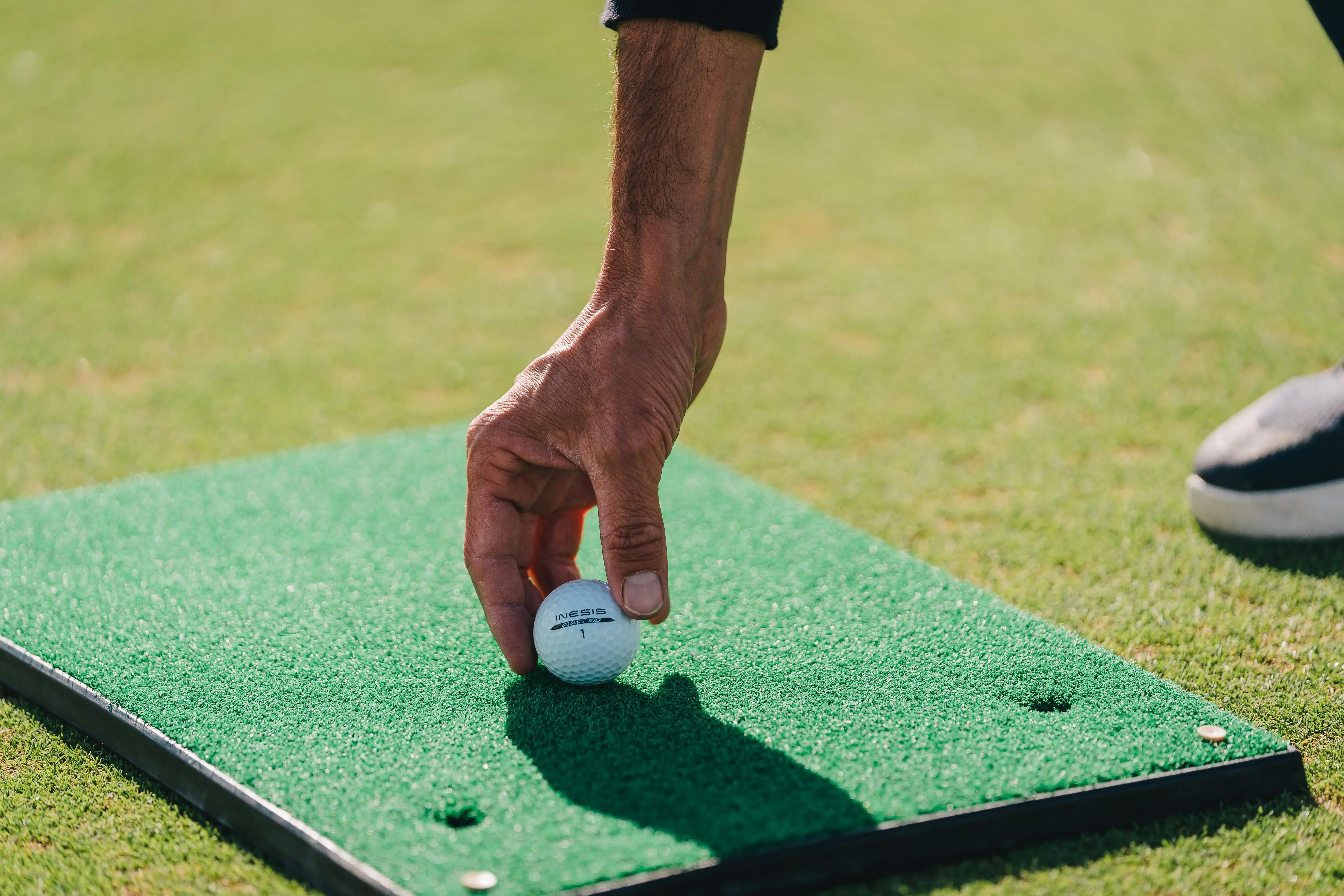 Hand placing a golf ball onto a green practice mat