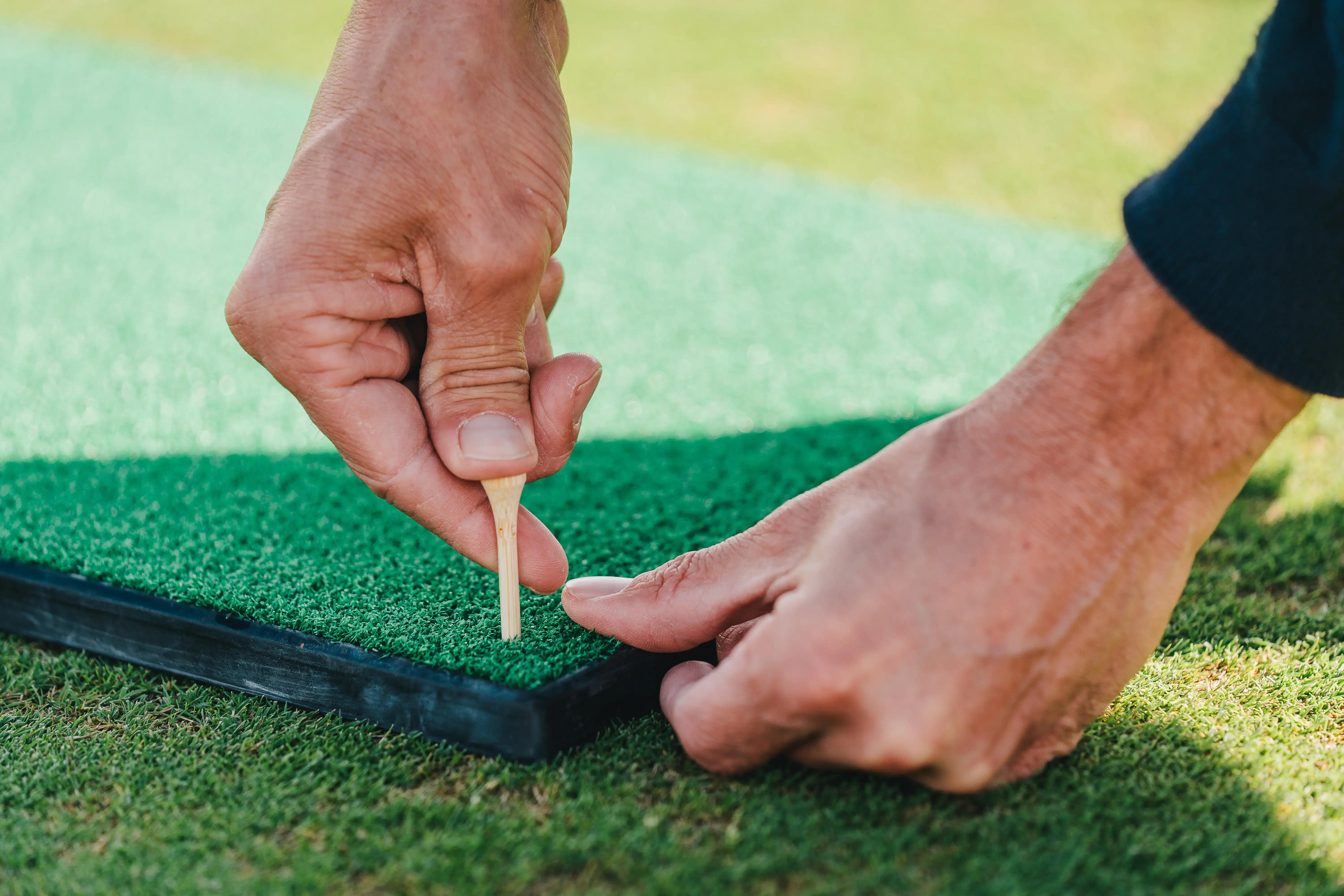 Hands placing a wooden tee into a green practice mat