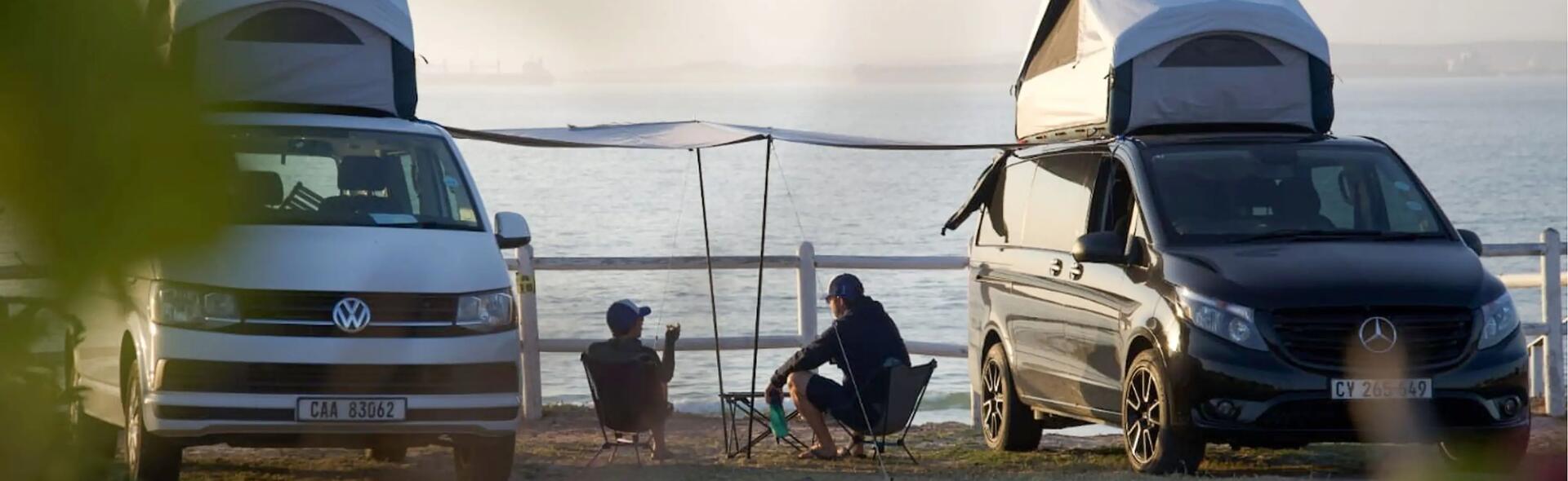 mężczyźni siedzący na krzesłach turystycznych obok zaparkowanych kamperów
