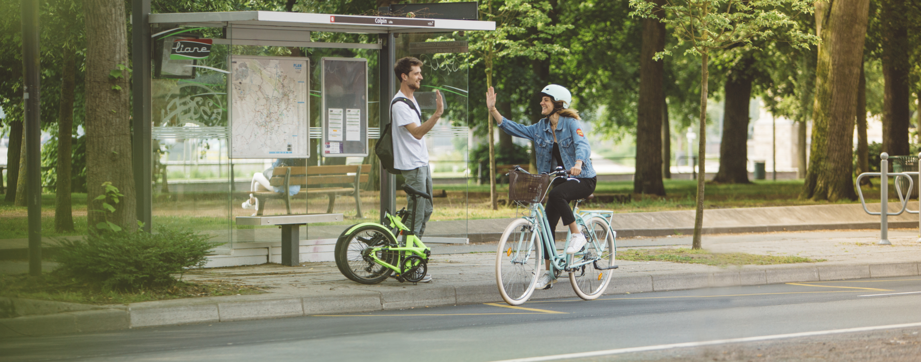 En kvinna cyklar förbi en man i en busskur och gör en high five - för att han också har en cykel med sig