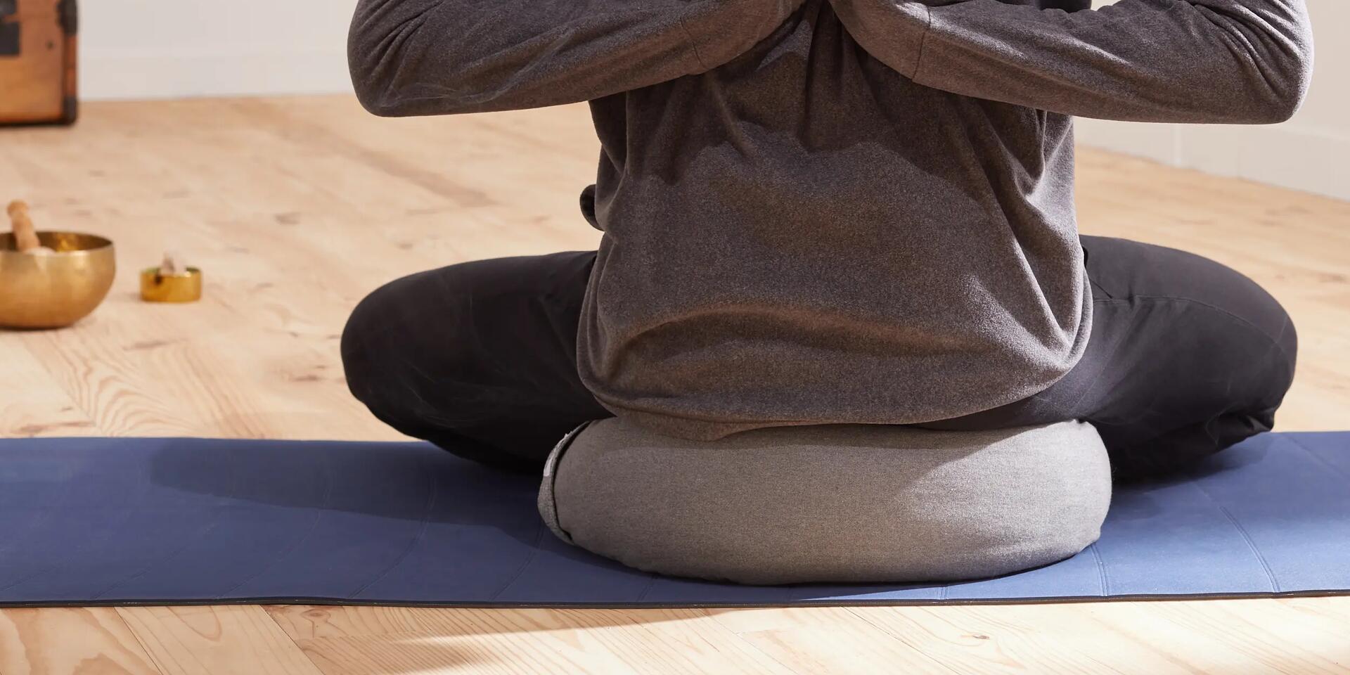 Rückansicht von einem Mann, der im Schneidersitz auf einem Yoga-Kissen sitzt