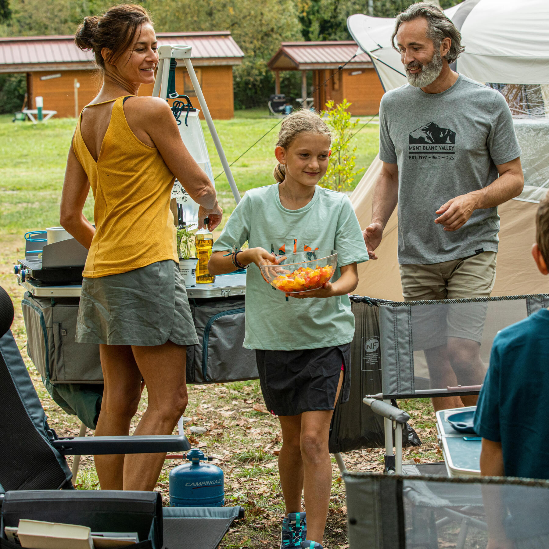 une femme, un homme et une jeune fille en train de préparer le déjeuner en camping