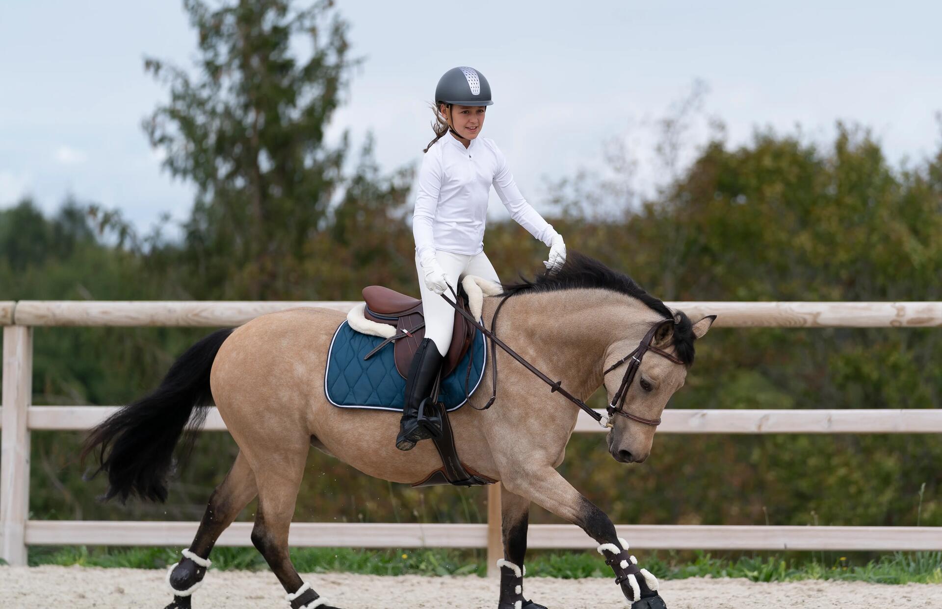 Kind reitet auf Pferd in weißem Reiteroutfit