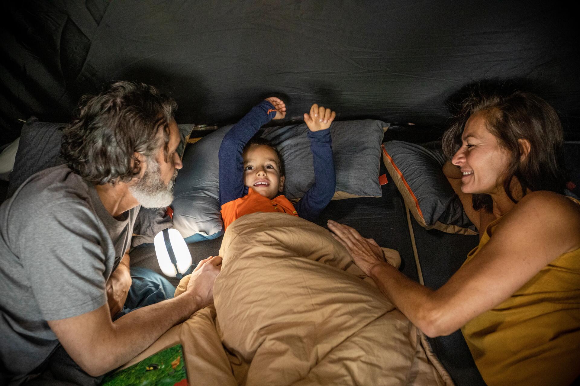 Familie liegt mit Campinglampe im Bett