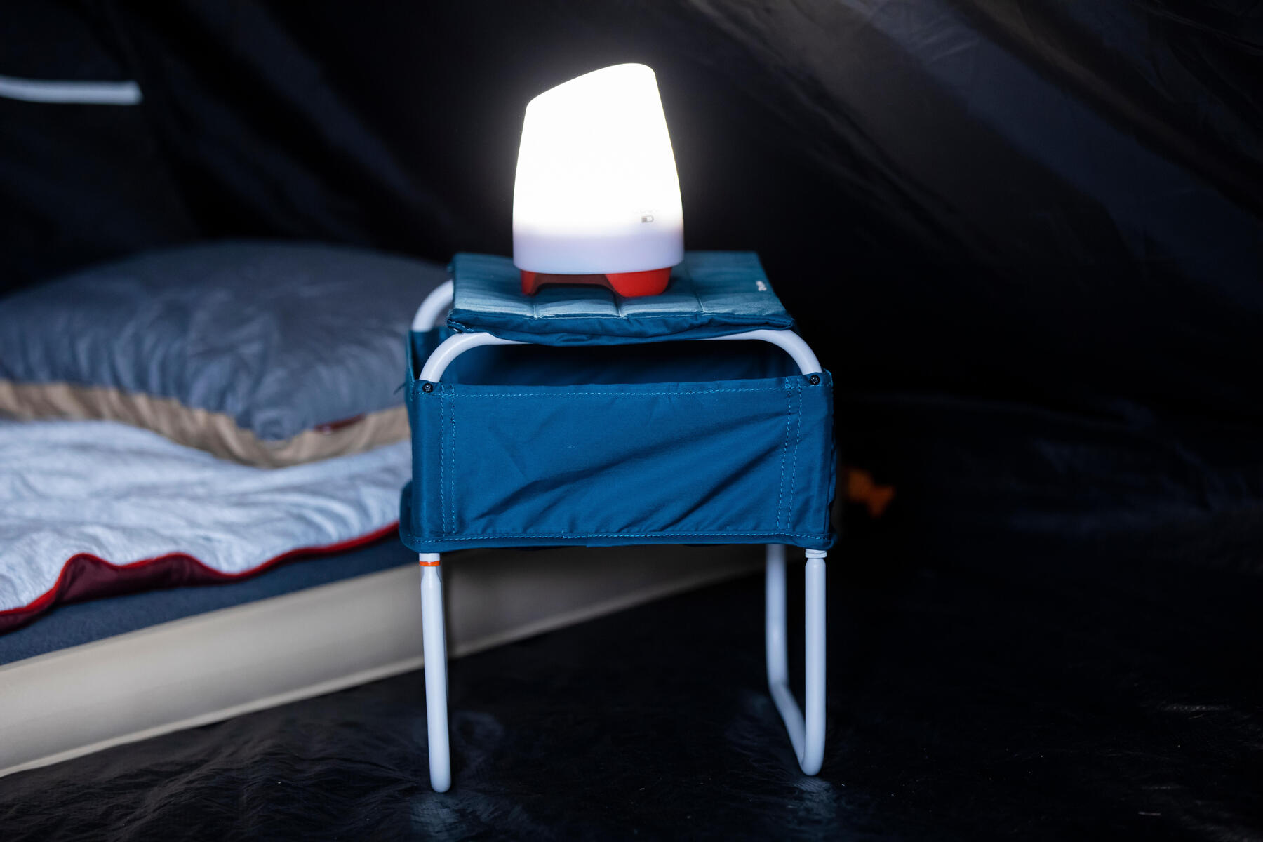 Campinglampe steht auf einem kleinen Tisch neben der Luftmatratze.