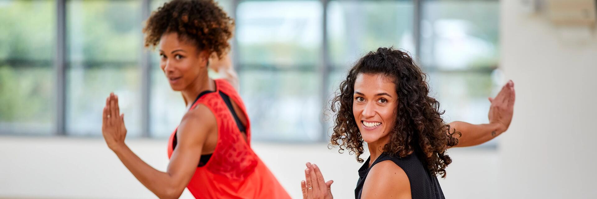 Uśmiechnięte kobiety w odzieży sportowej pokazujące co to jest zumba na sali treningowej