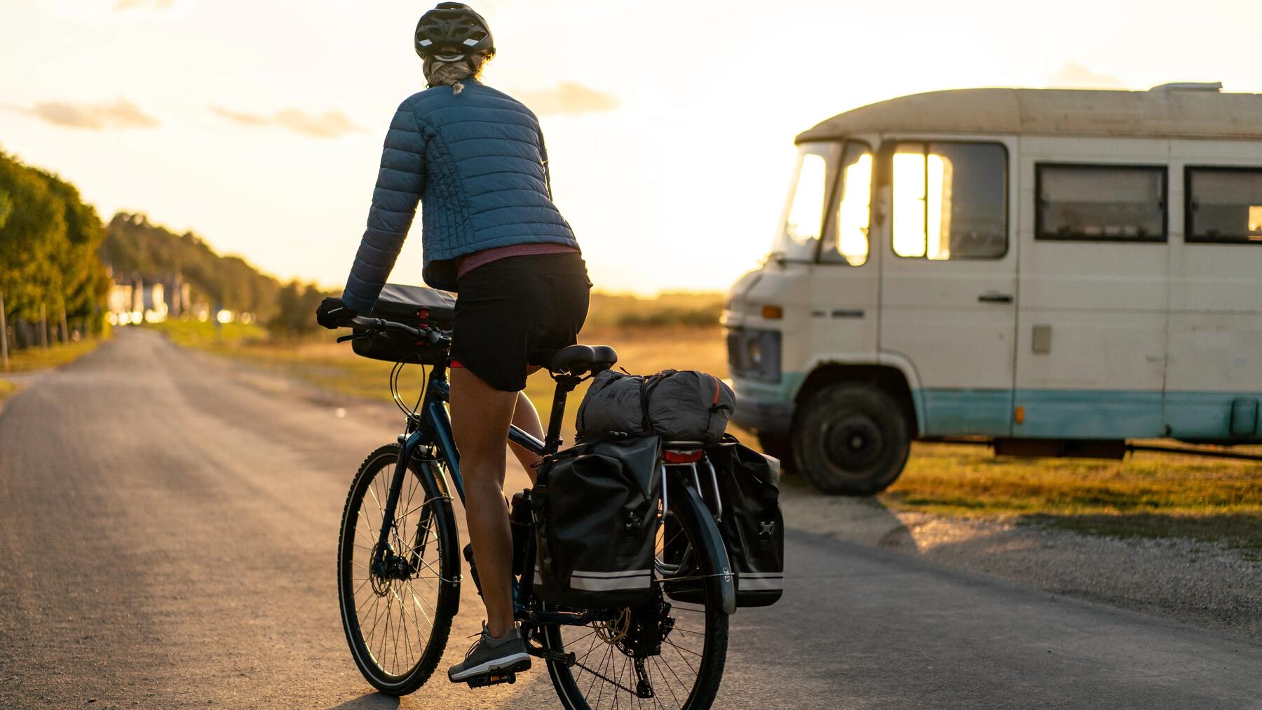 Kobieta w kasku rowerowym jadąca na rowerze z zamontowanymi sakwami rowerowymi