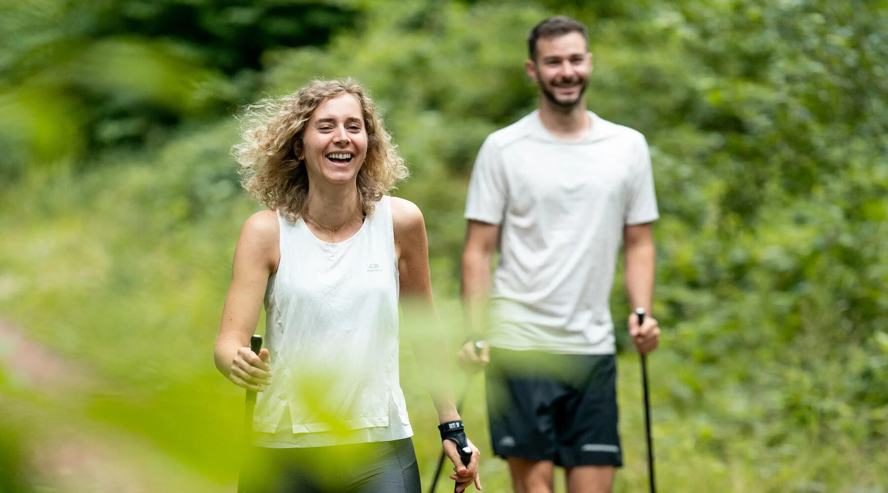 Mann und Frau wandern mit Nordic Walking Stöcken auf einem Waldweg.