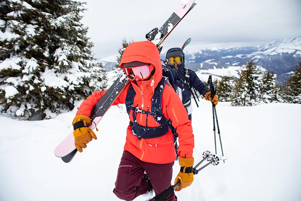 Zwei Freeride-Skifahrer mit bunter Skibekleidung laufen durch Schneelandschaft.