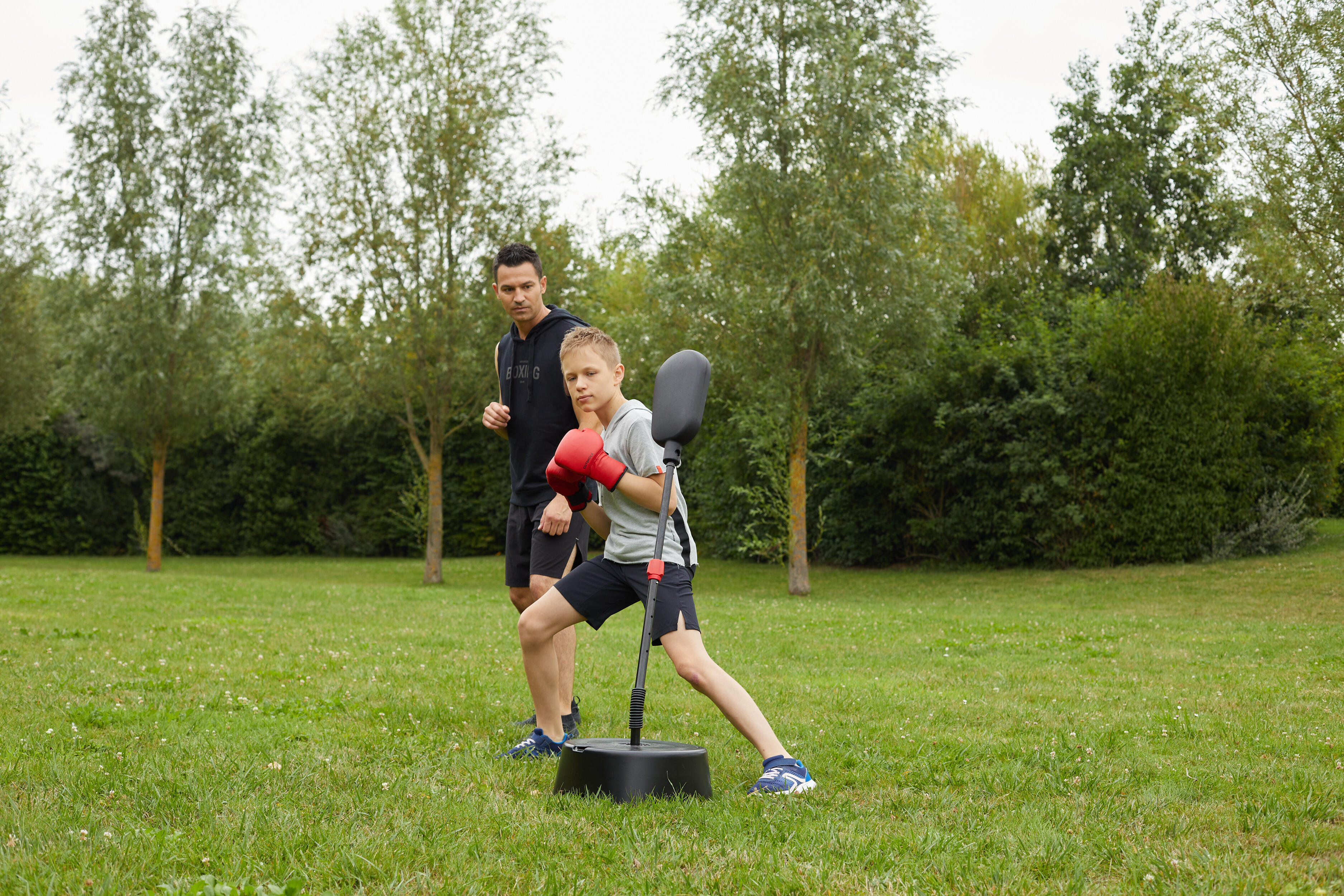 Child wearing red boxing gloves training with a freestanding reflex punching bag outdoors