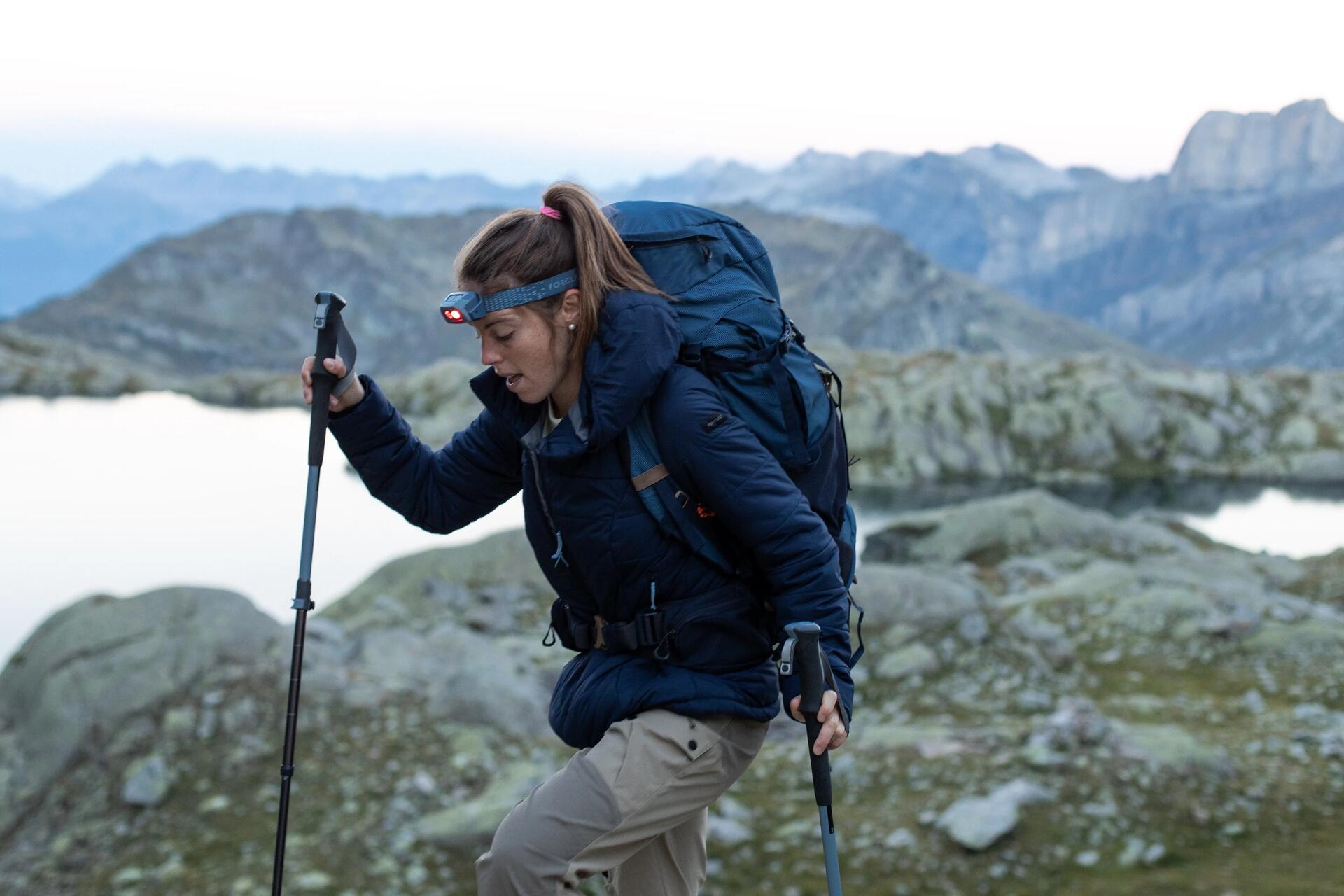 kobieta z czołówką na głowie wędrująca po górach trzymając kijki trekkingowe w rękach